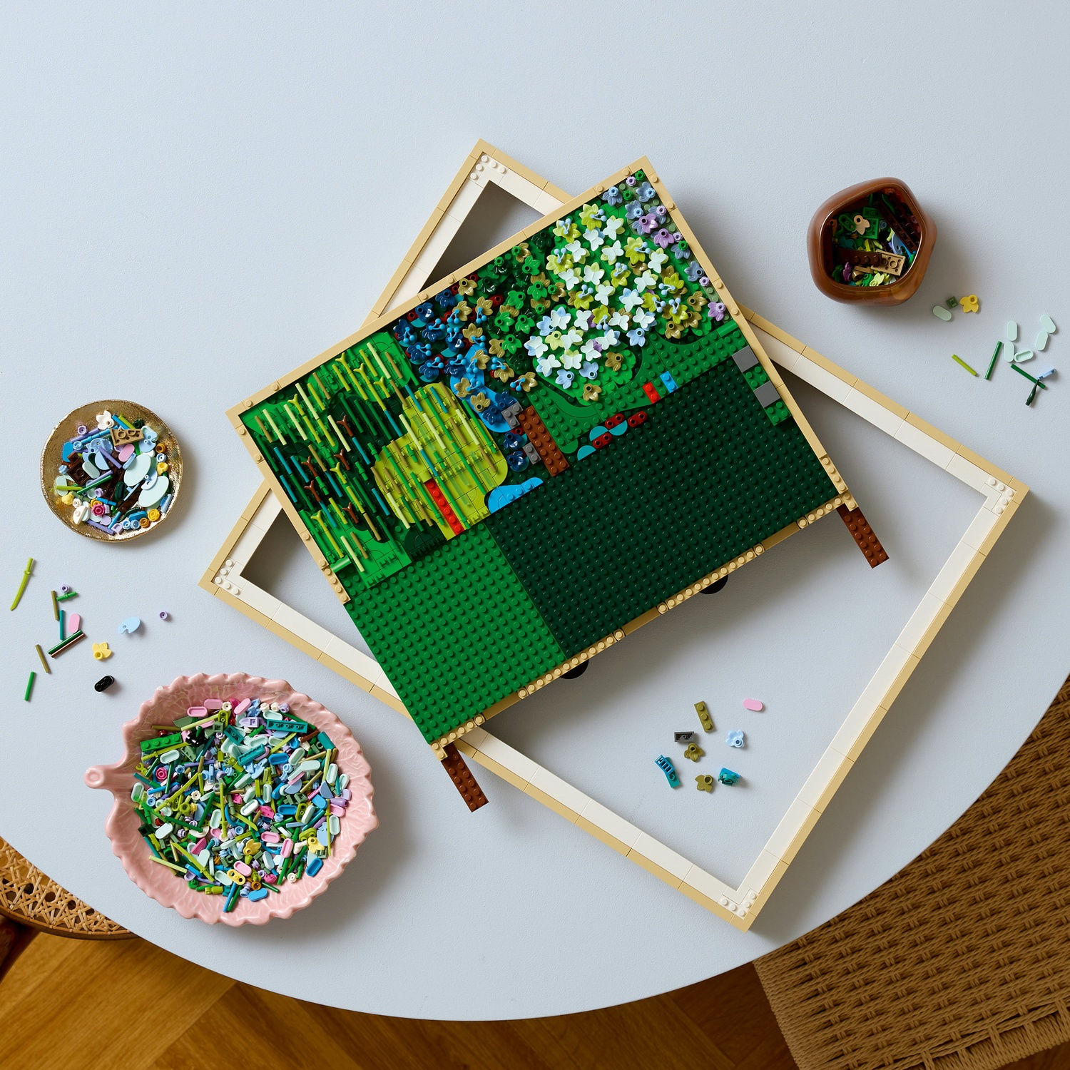 Una scena di giardino Lego parzialmente costruita con mattoncini sparsi e ciotole di smistamento su un tavolo.