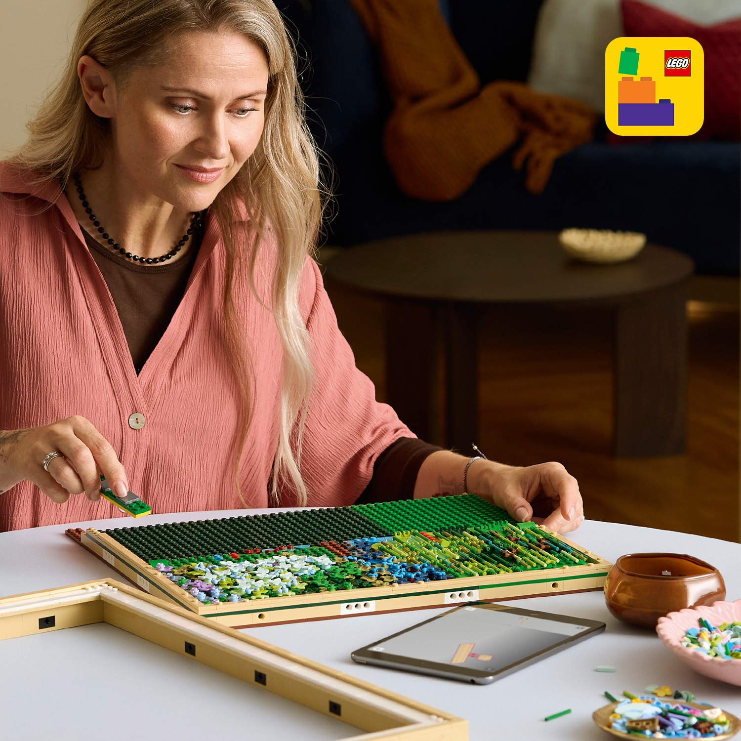 Una donna costruisce un mosaico LEGO con fiori e alberi verdi.