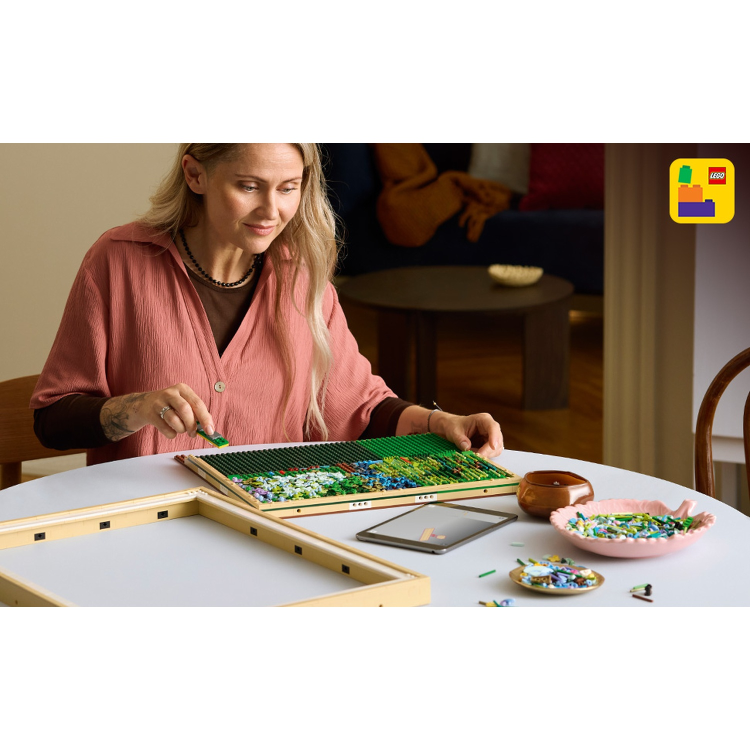 Donna che costruisce un mosaico floreale Lego con tessere verdi, blu e bianche.