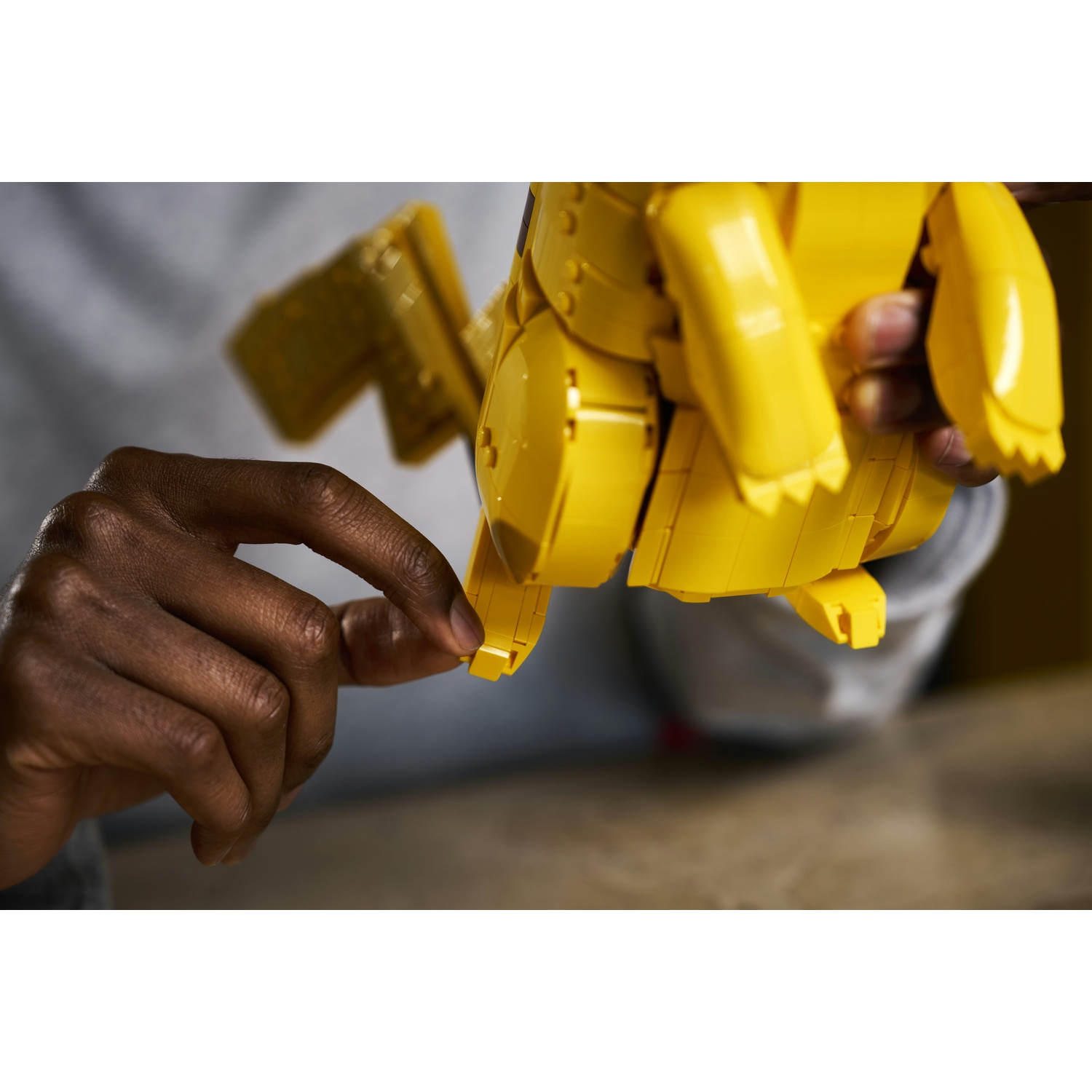Una mano assembla pezzi LEGO gialli in un modello di Pikachu.