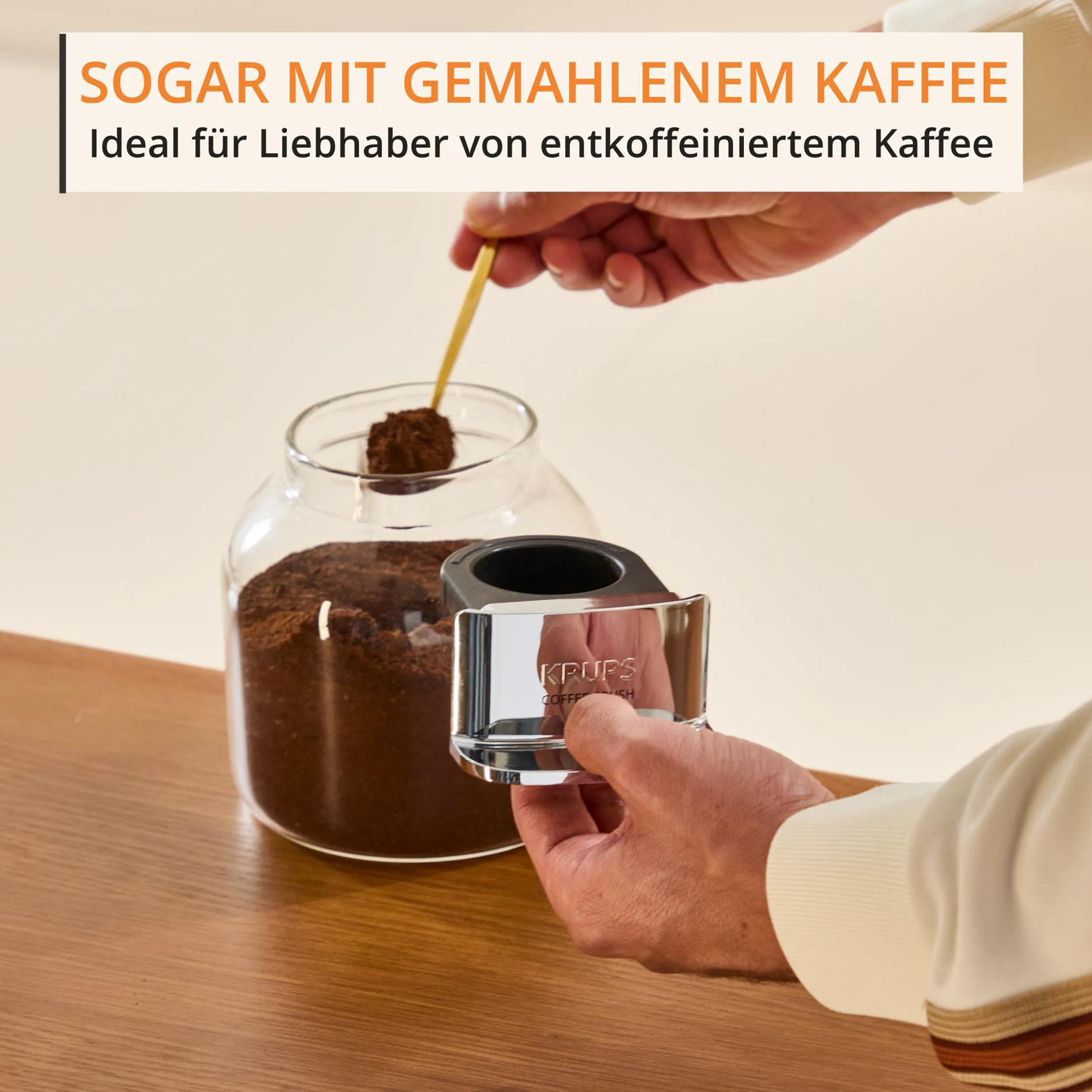 Eine Hand entnimmt Kaffeepulver mit einem Löffel aus einem Glas.