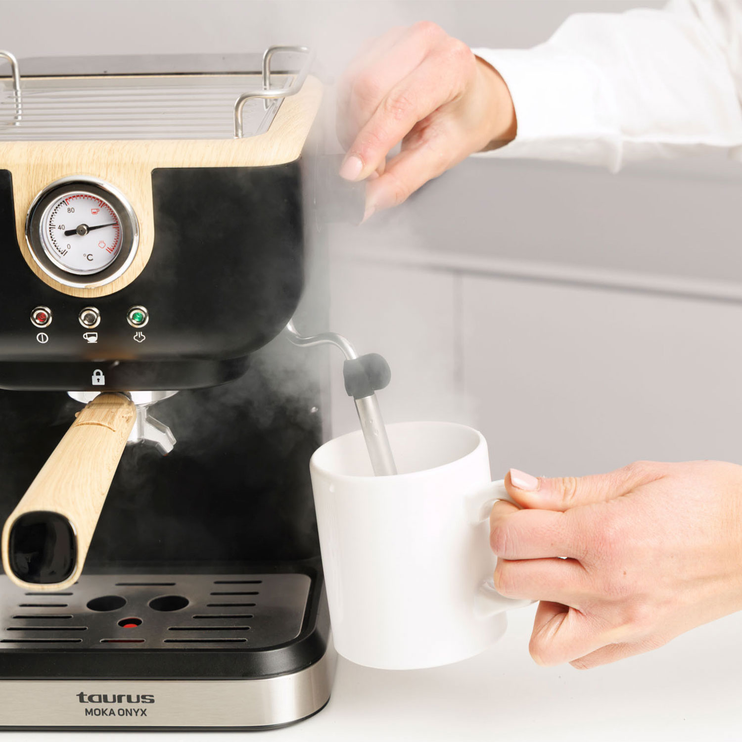 Una persona usa una cafetera, dirigiendo vapor a una taza blanca.