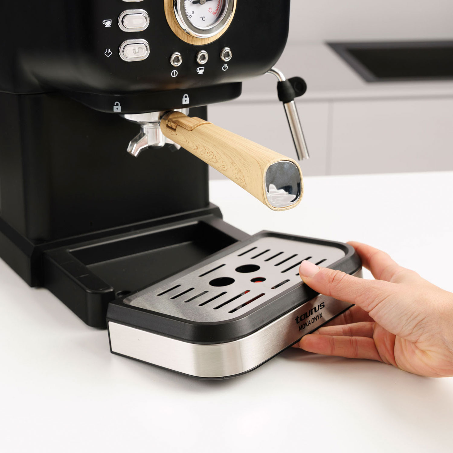 Una mano desliza una bandeja de goteo bajo una máquina de espresso.
