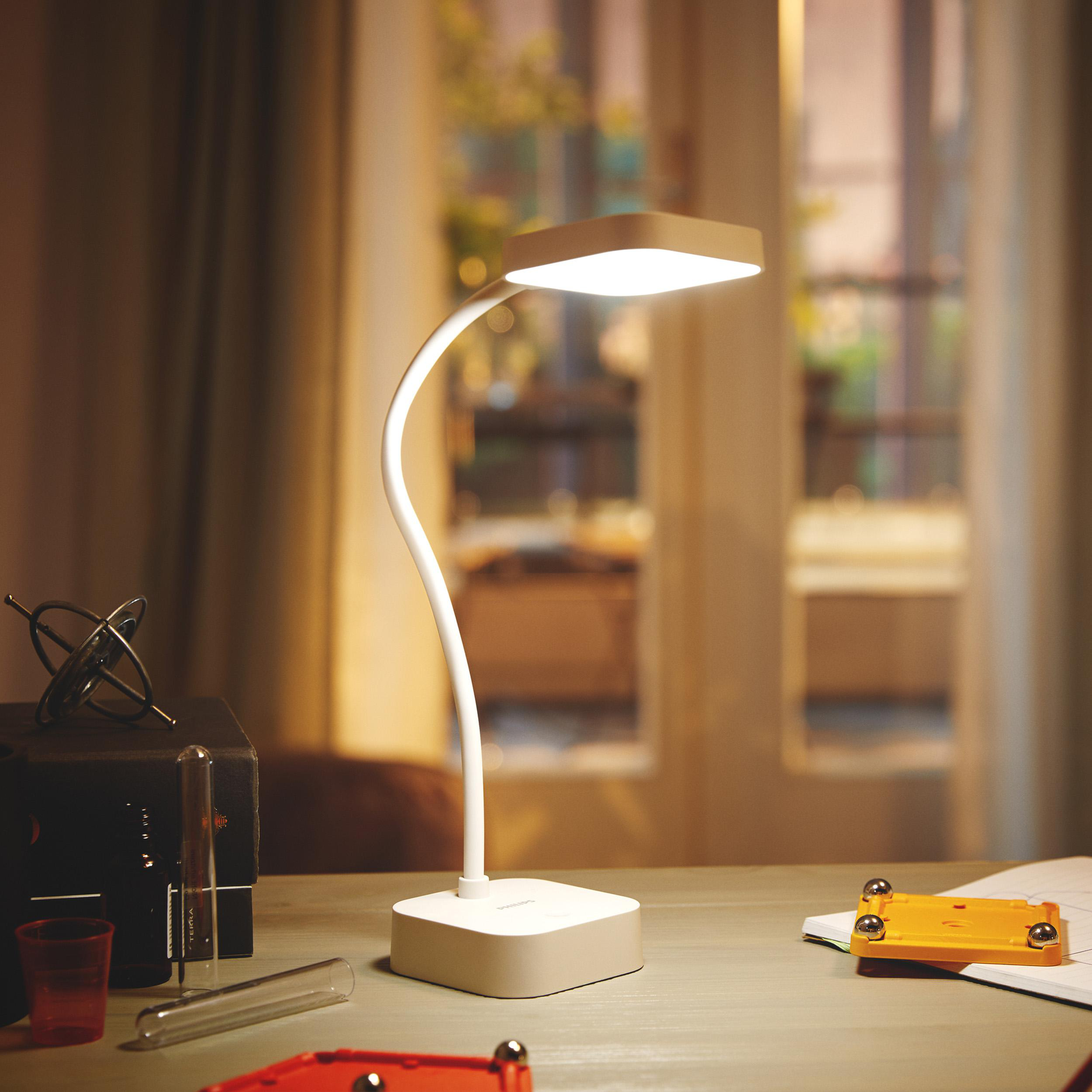 Eine weiße Schreibtischlampe leuchtet auf einem Holztisch neben wissenschaftlichen Geräten.