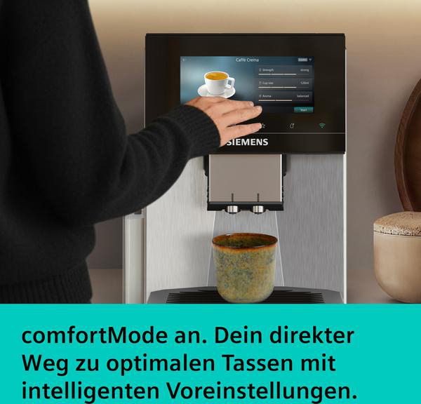 Eine Hand bedient ein Siemens Kaffeevollautomat-Display. Eine Tasse steht bereit.