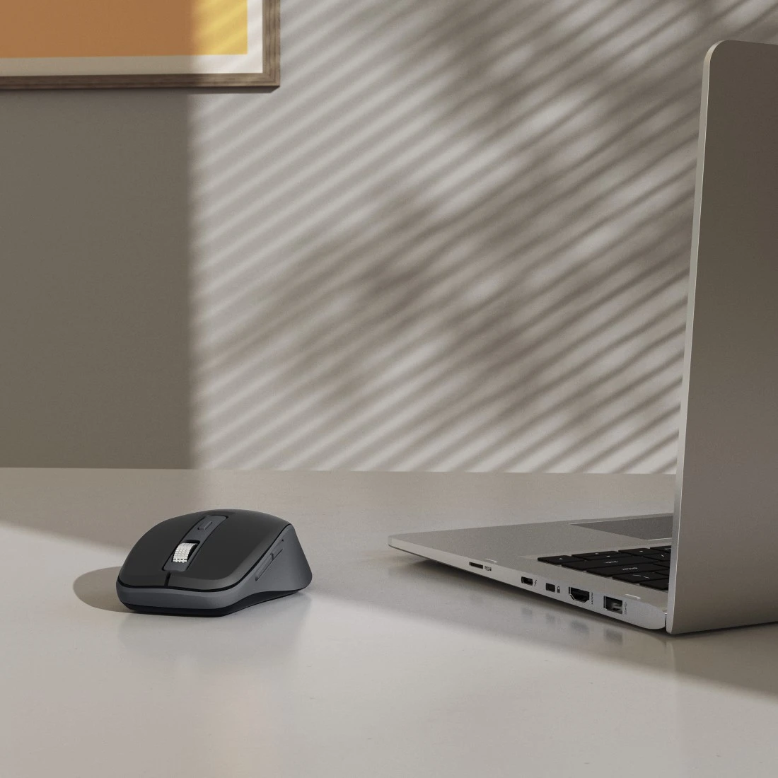 Ciemna mysz leży na lewo od laptopa na jasnym biurku.