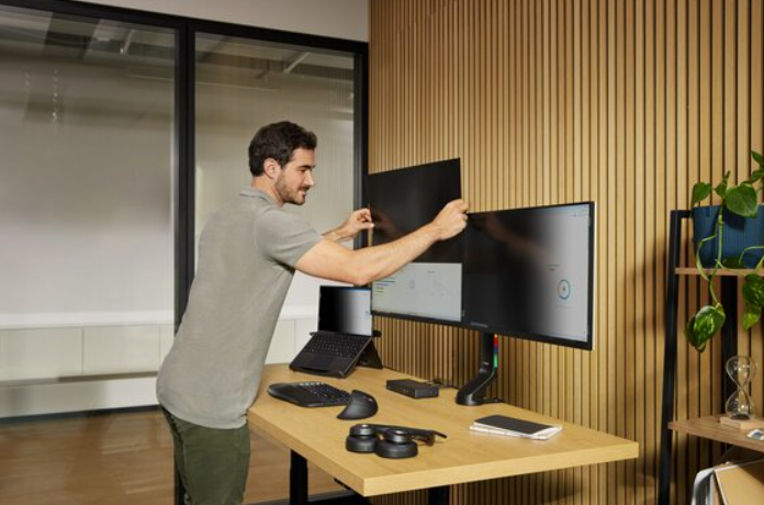 Mann stellt Monitore auf dem Schreibtisch ein.