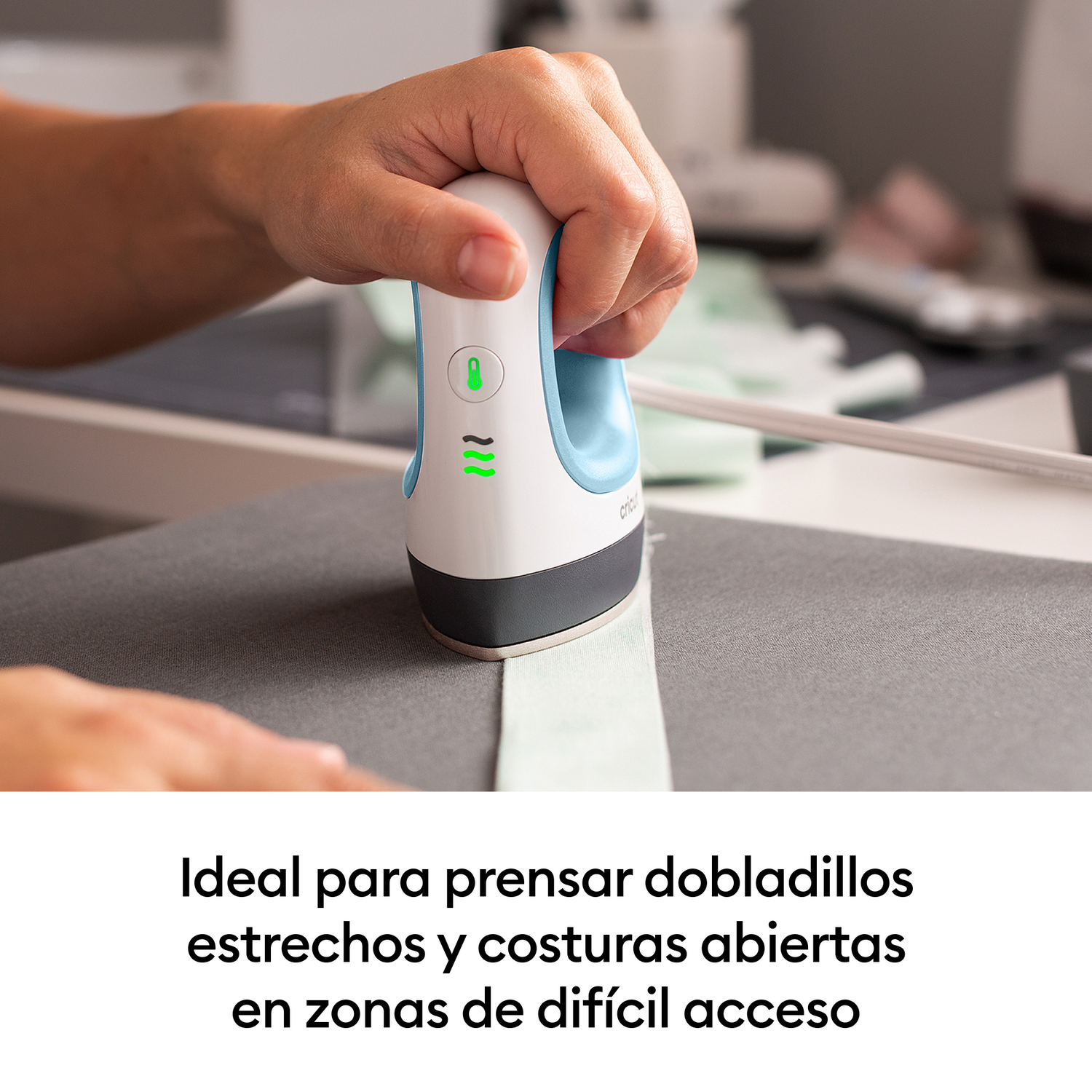 Una mano sostiene una plancha pequeña sobre tela. Primer plano.