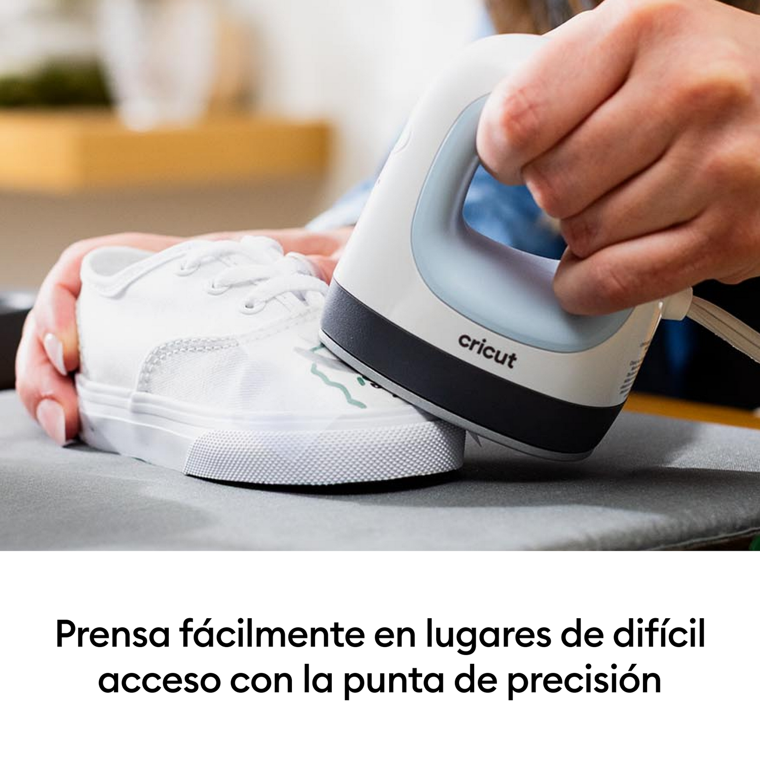 Una mano sostiene una prensa térmica blanca sobre una zapatilla de lona blanca.