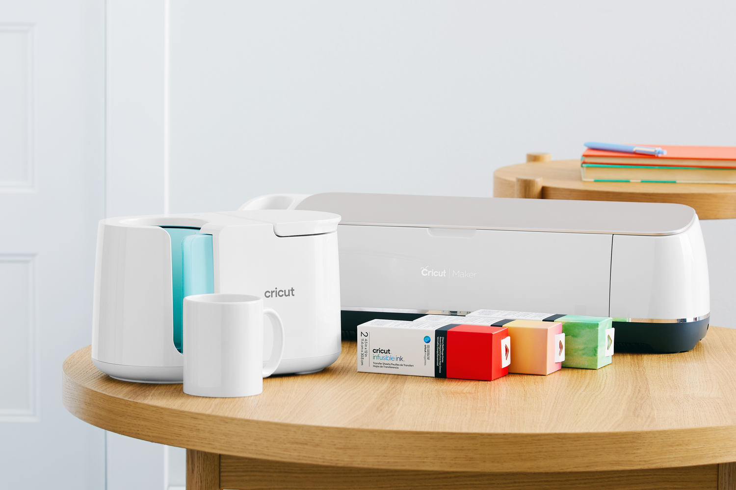 Cricut Maker, prensa de tazas, taza blanca y cartuchos Infusible Ink en mesa madera.