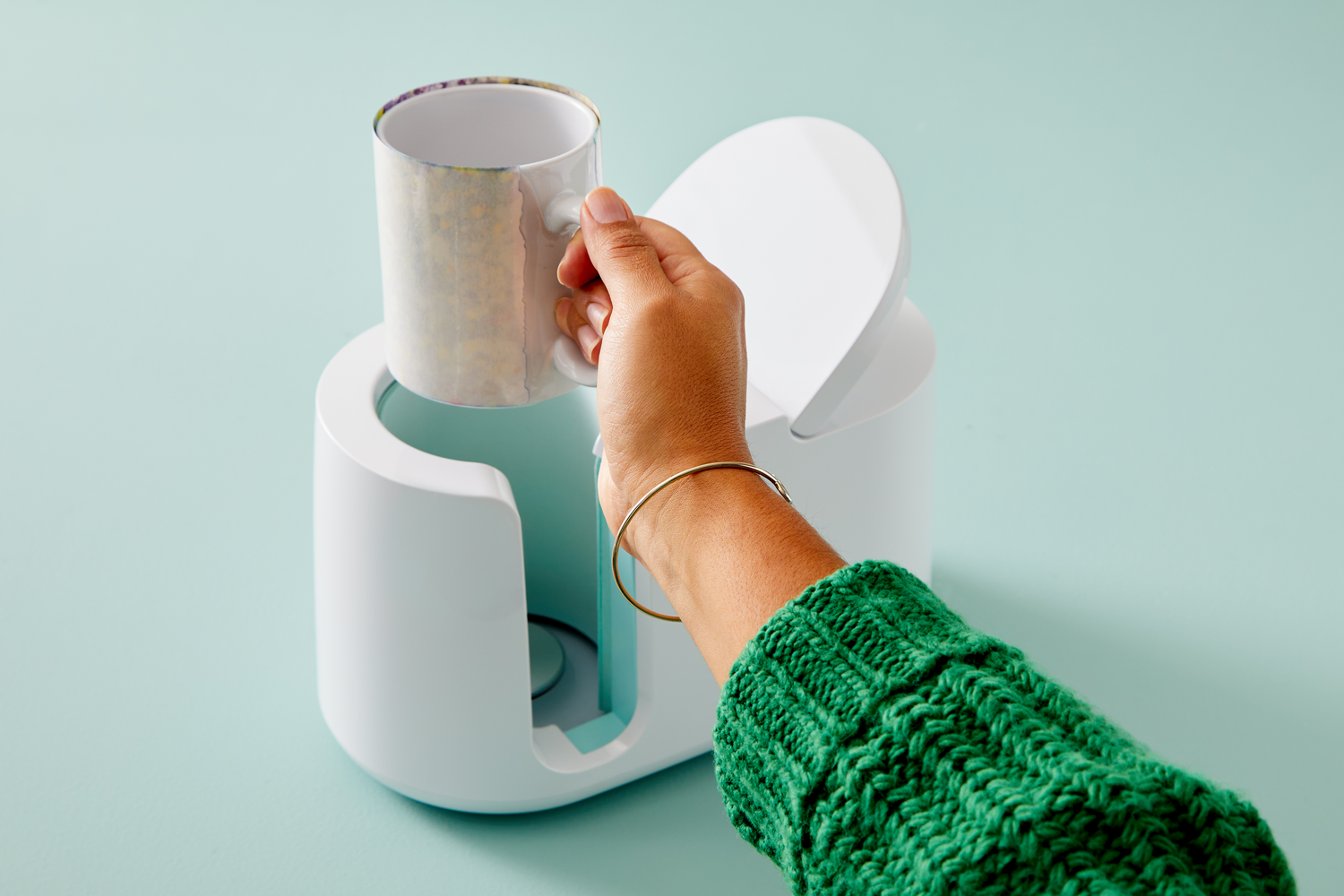 Una mano con pulsera dorada coloca una taza impresa en una máquina blanca.