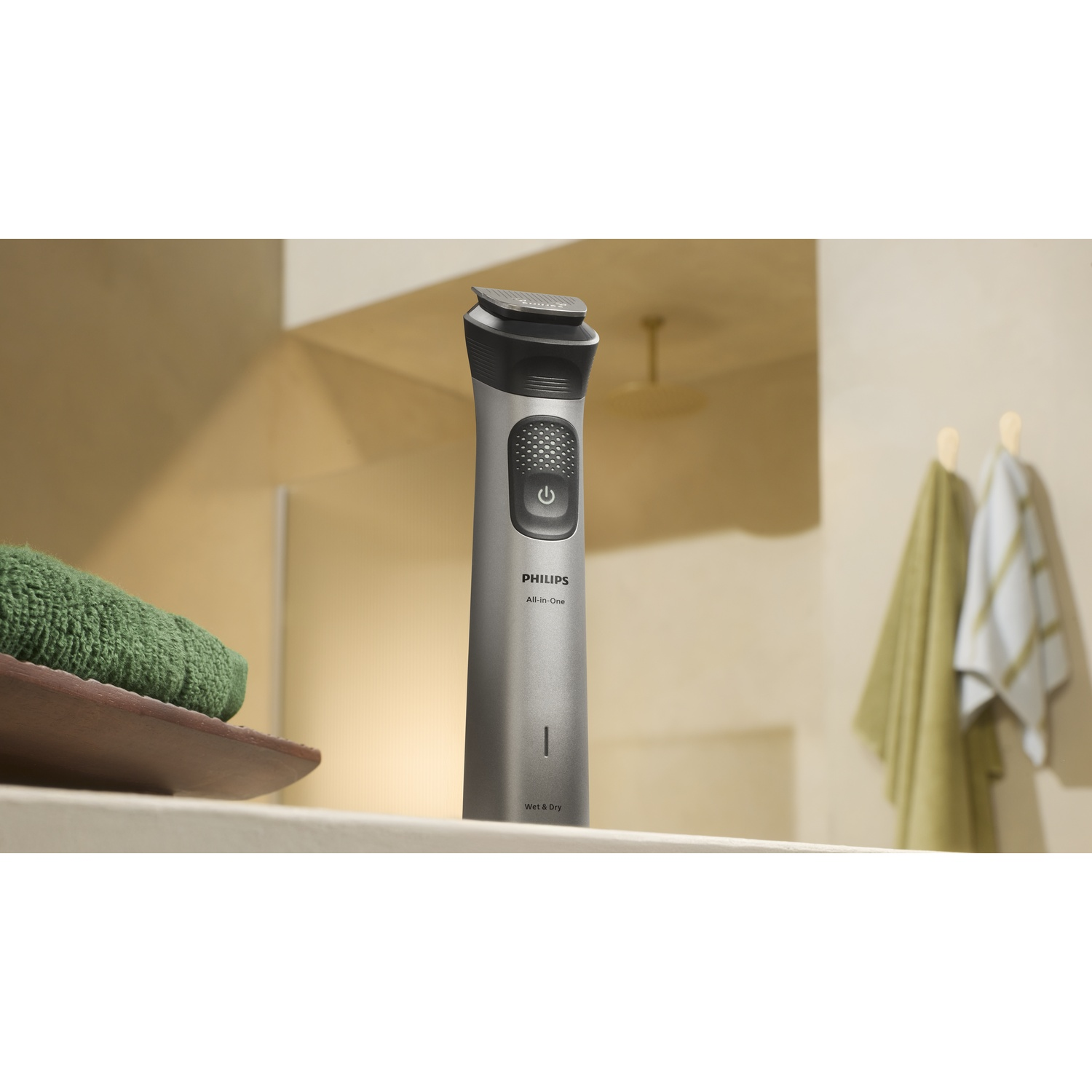 Un rifinitore Philips All-in-One argentato con pulsante di accensione su uno scaffale. Asciugamano verde a sinistra.