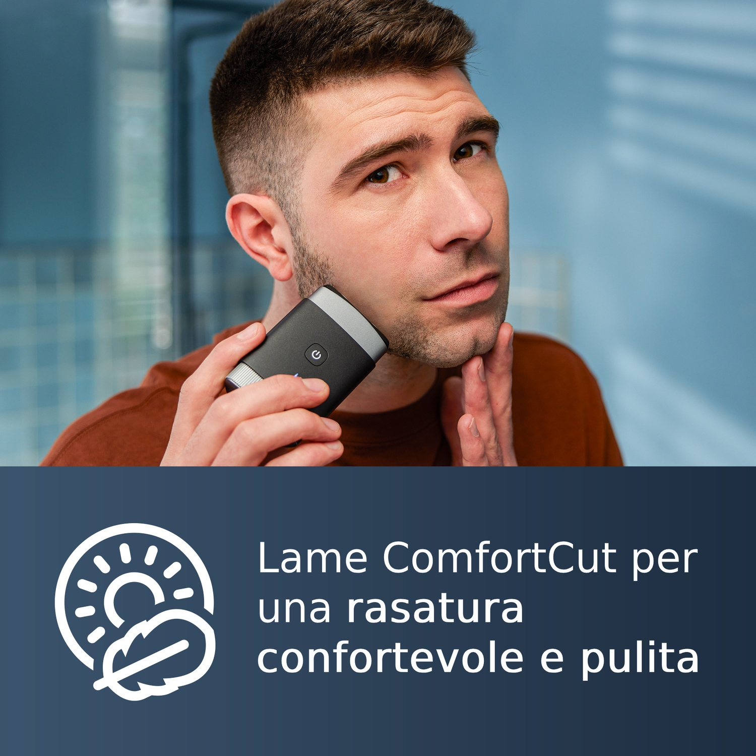 Uomo si rade con un rifinitore nero. Lo sfondo è piastrellato di blu.