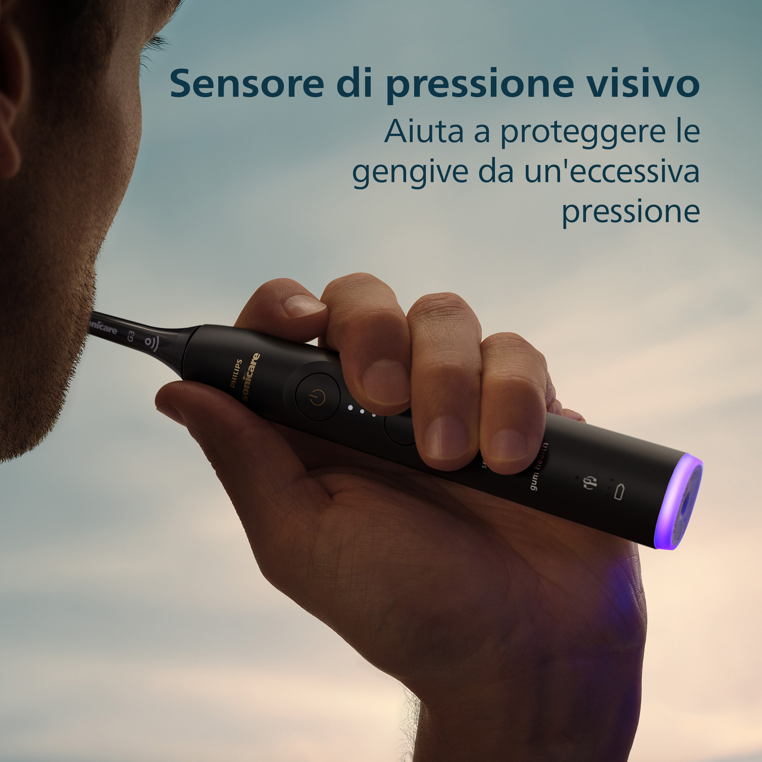 Una mano tiene uno spazzolino elettrico nero con luce viola alla fine. Il cielo è sullo sfondo.