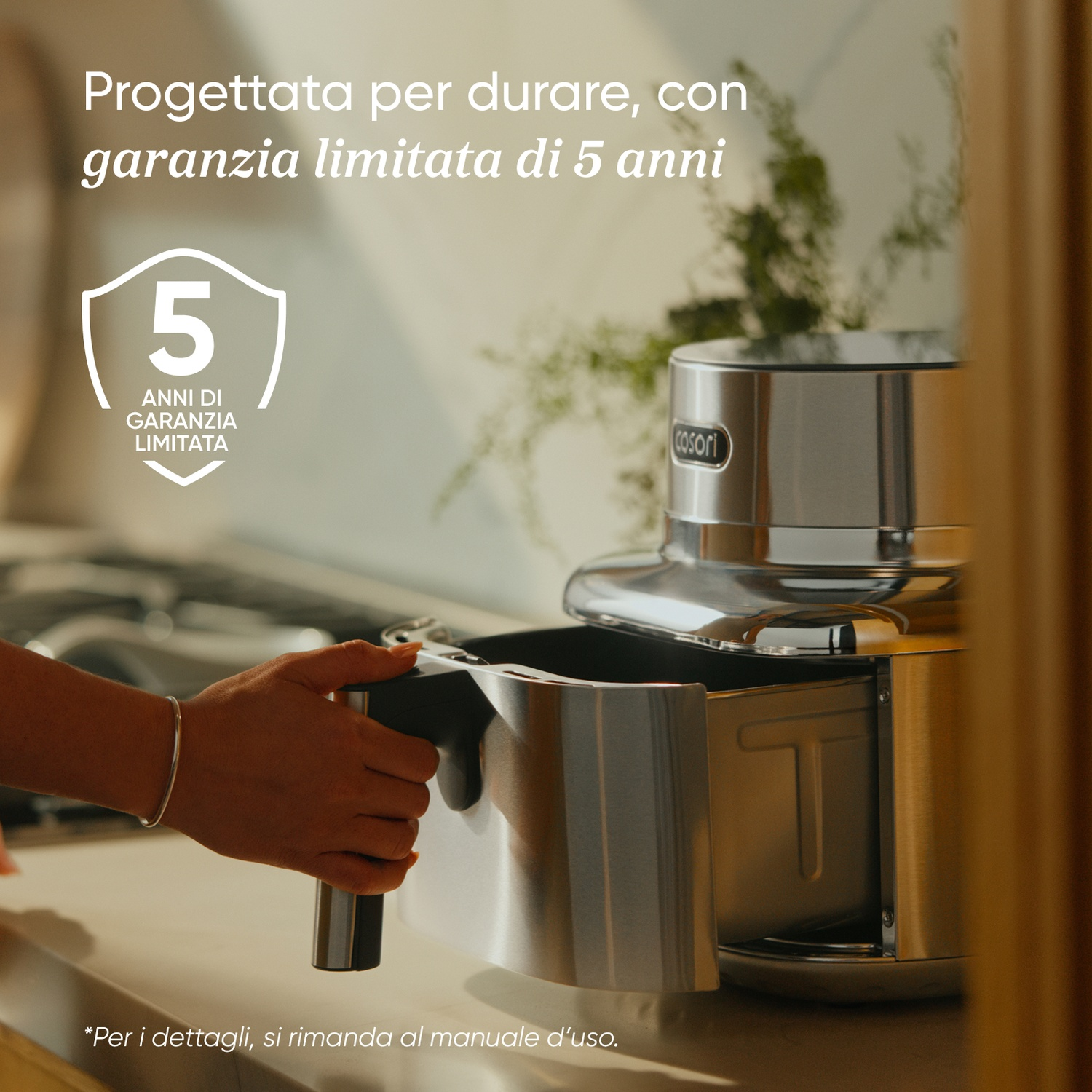 Una mano estrae il cestello di una friggitrice ad aria argentata. Garanzia 5 anni.