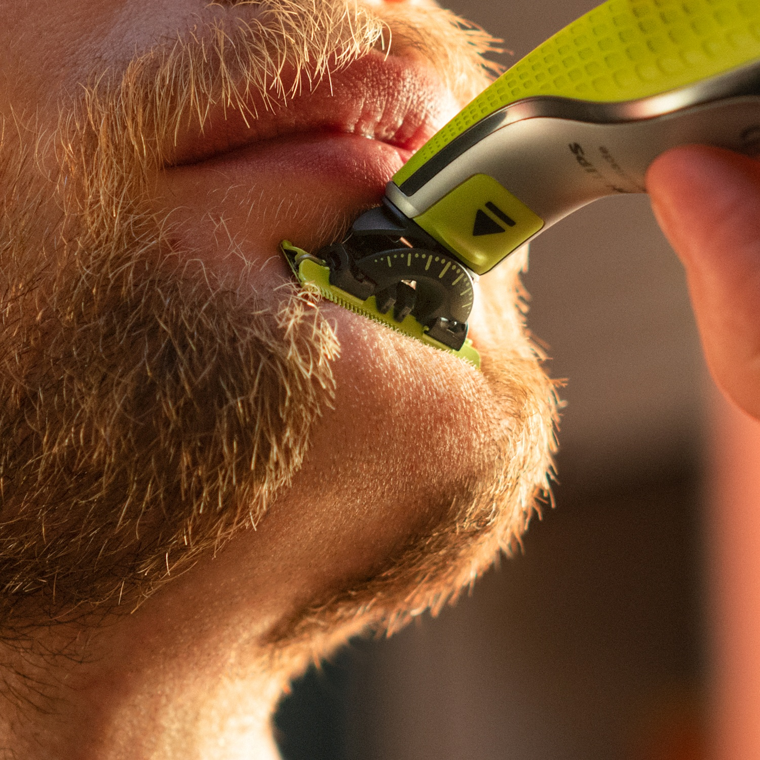 Uomo si taglia la barba con rifinitore elettrico, primo piano.