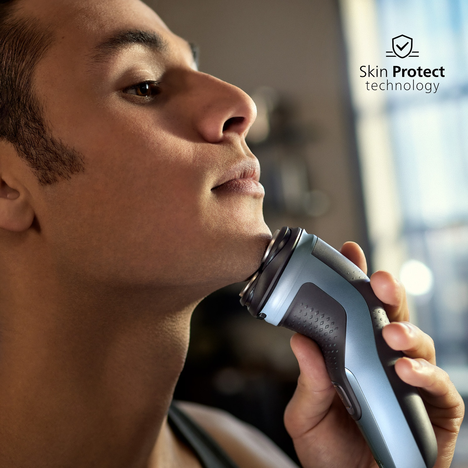 Primo piano di un uomo che si rade il viso con un rasoio elettrico blu e grigio. Testo Skin Protect.