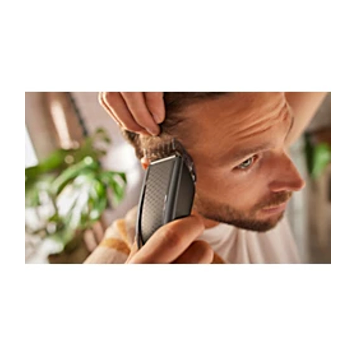 Uomo si taglia i capelli con un tagliacapelli, pianta sullo sfondo.