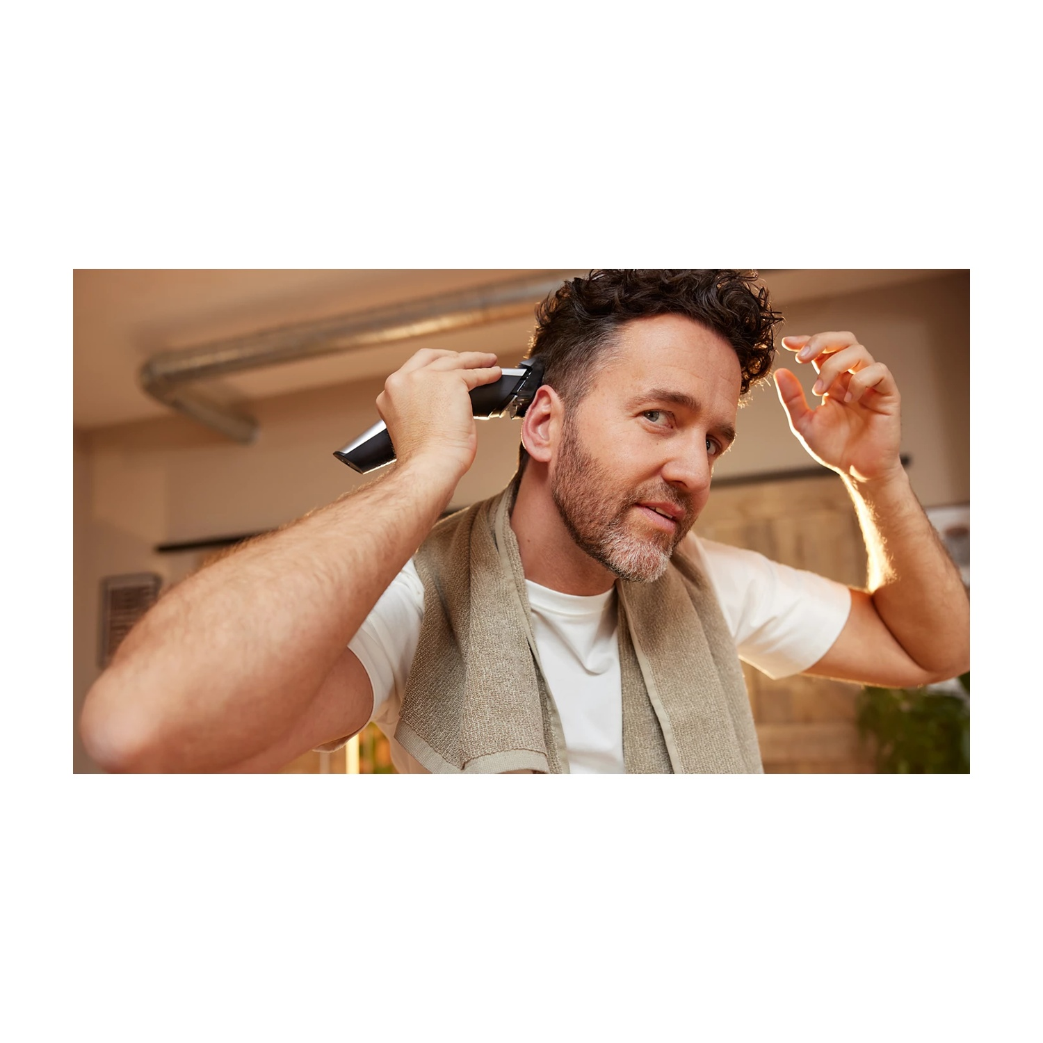Uomo con capelli ricci si taglia i capelli con un tagliacapelli. Asciugamano al collo.