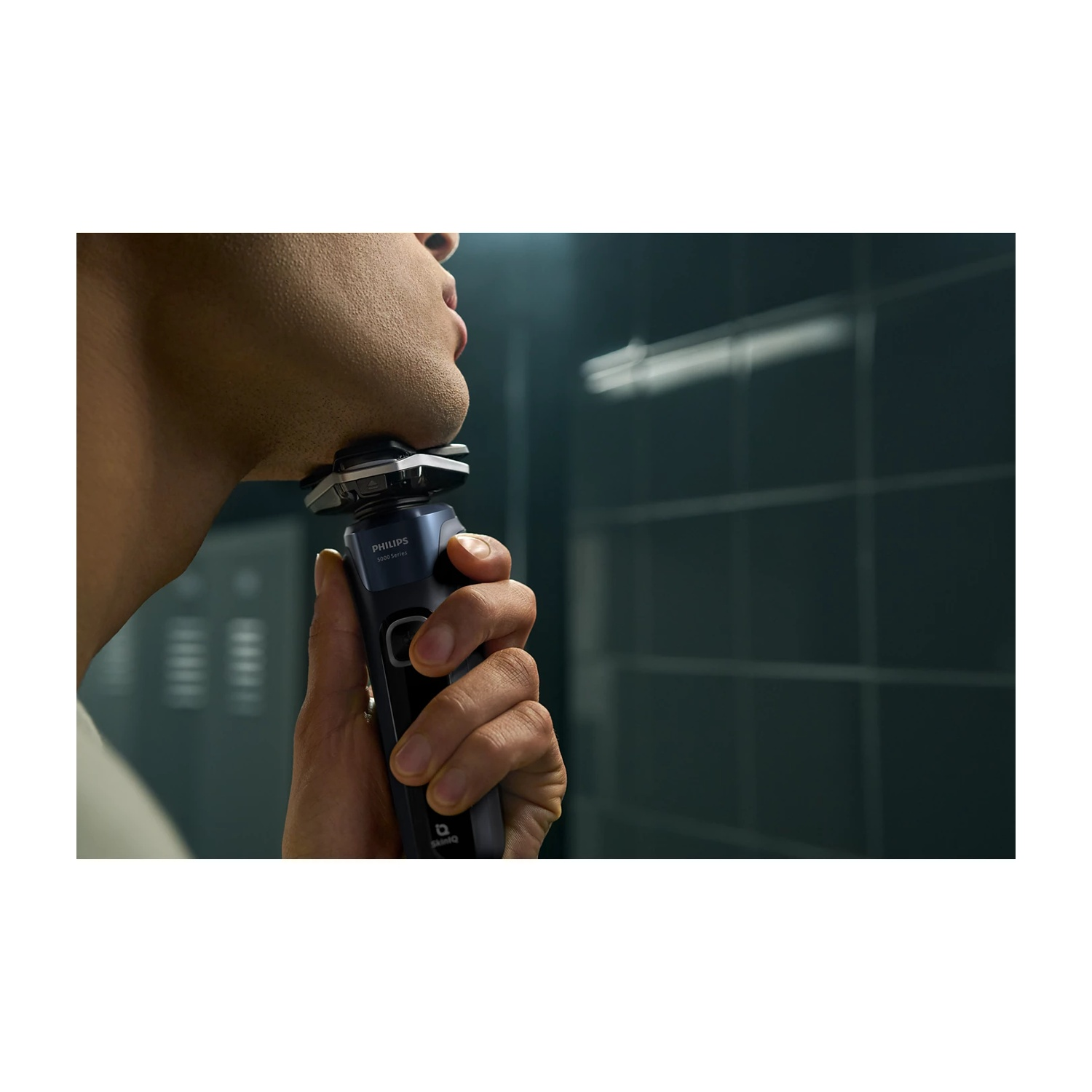 Uomo che si rade il viso con un rasoio elettrico Philips blu scuro.