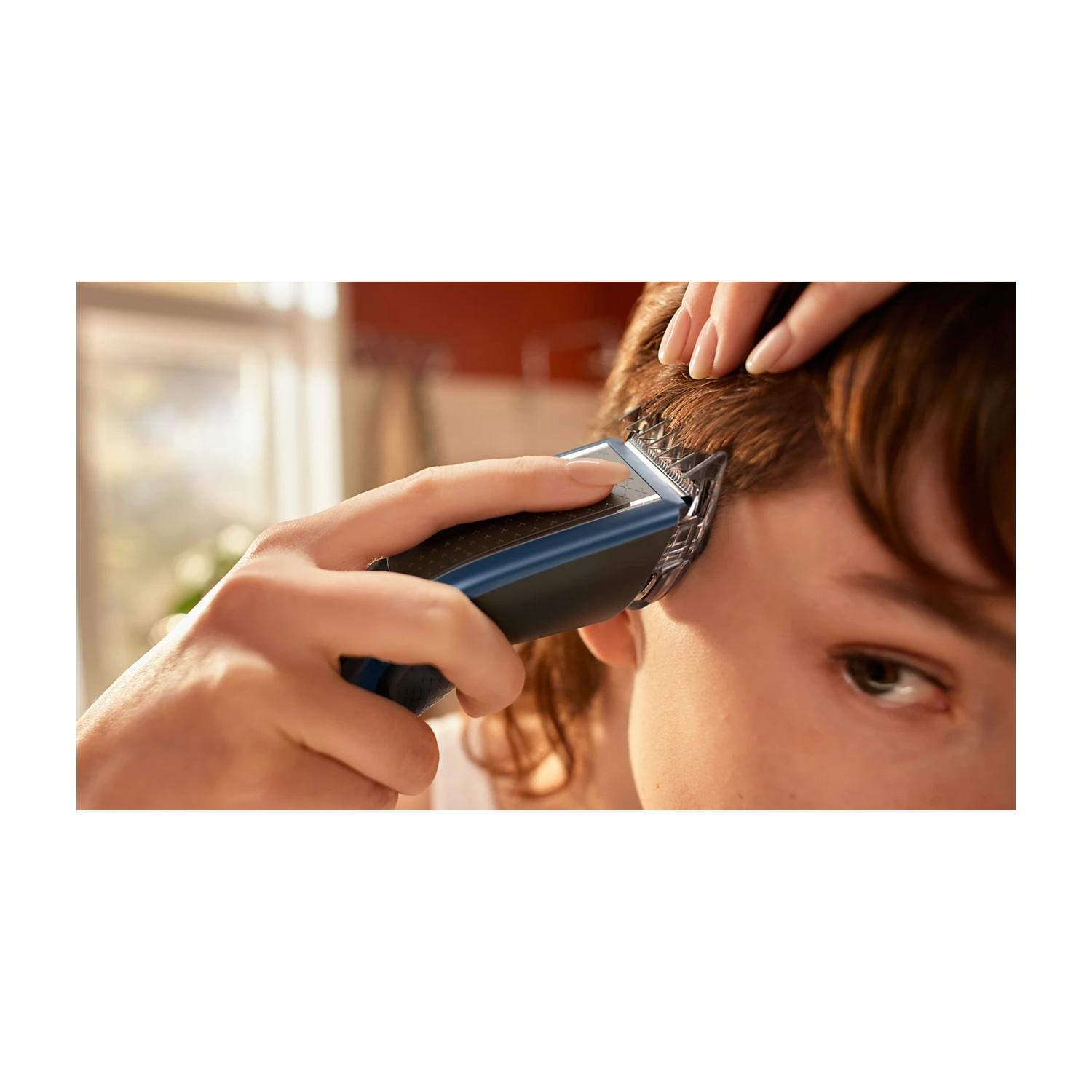 Una mano usa un tagliacapelli blu per tagliare capelli castani corti.