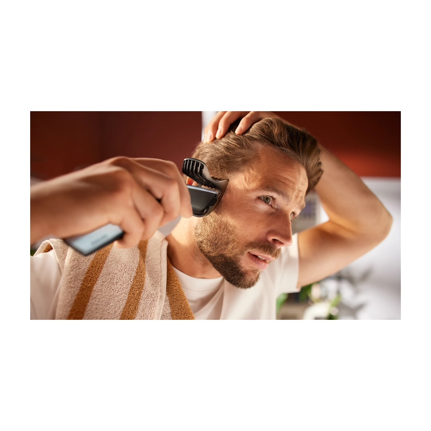 Uomo si taglia i capelli con rifinitore, mano in testa, asciugamano collo.