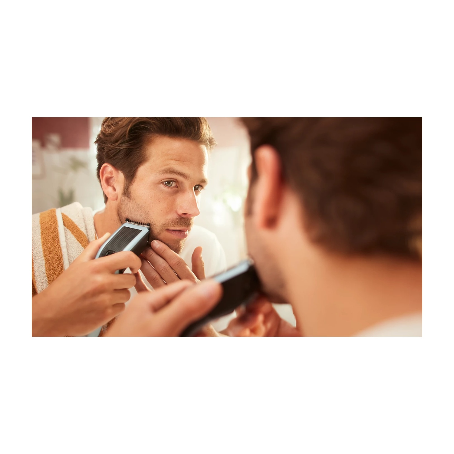 Uomo si taglia la barba allo specchio con un regolabarba elettrico.