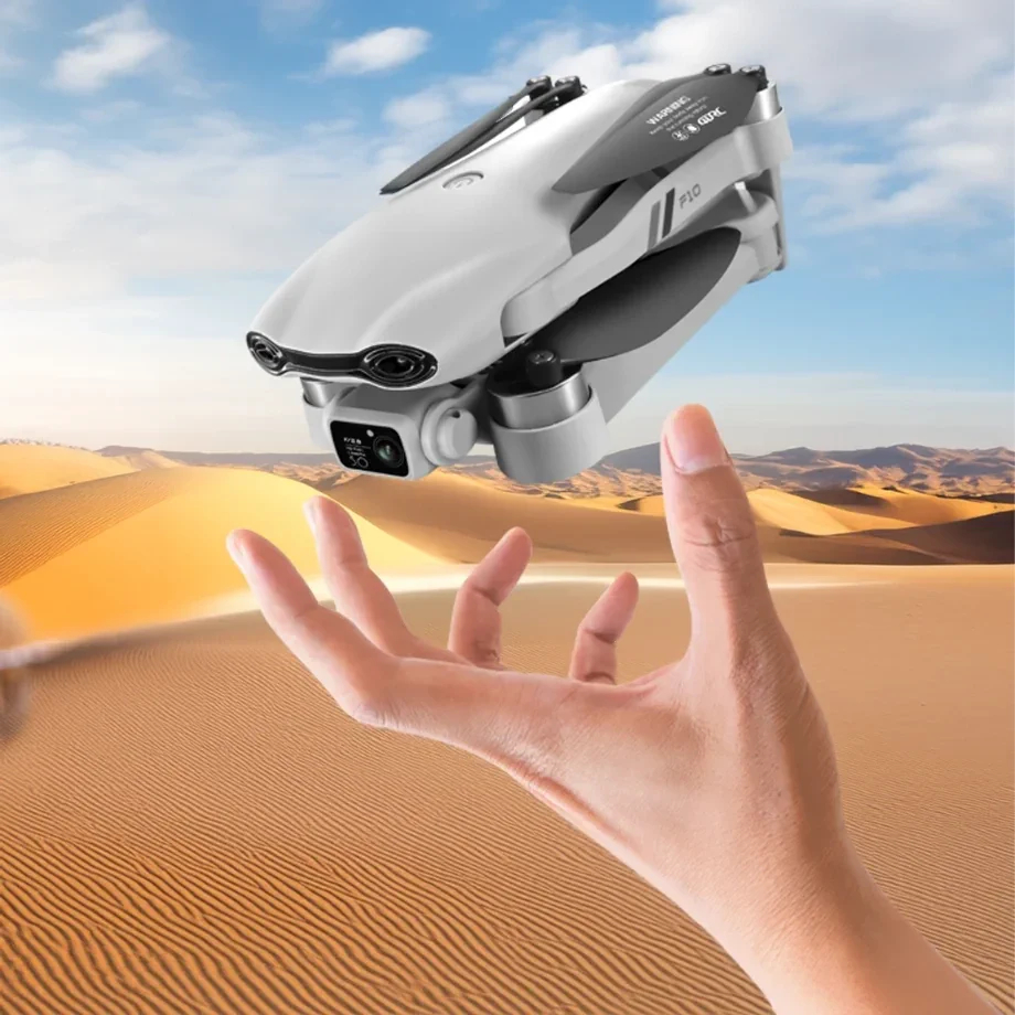 Biały dron unosi się nad dłonią na tle pustynnego krajobrazu.