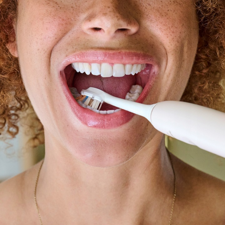 Kobieta myje zęby szczoteczką elektryczną.