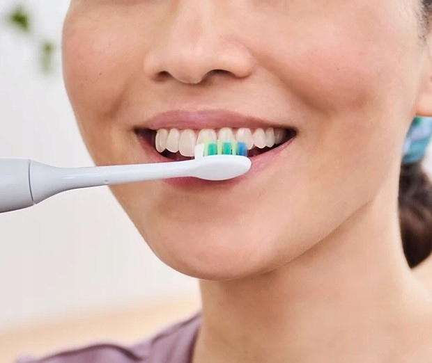 Kobieta myje zęby szczoteczką elektryczną.