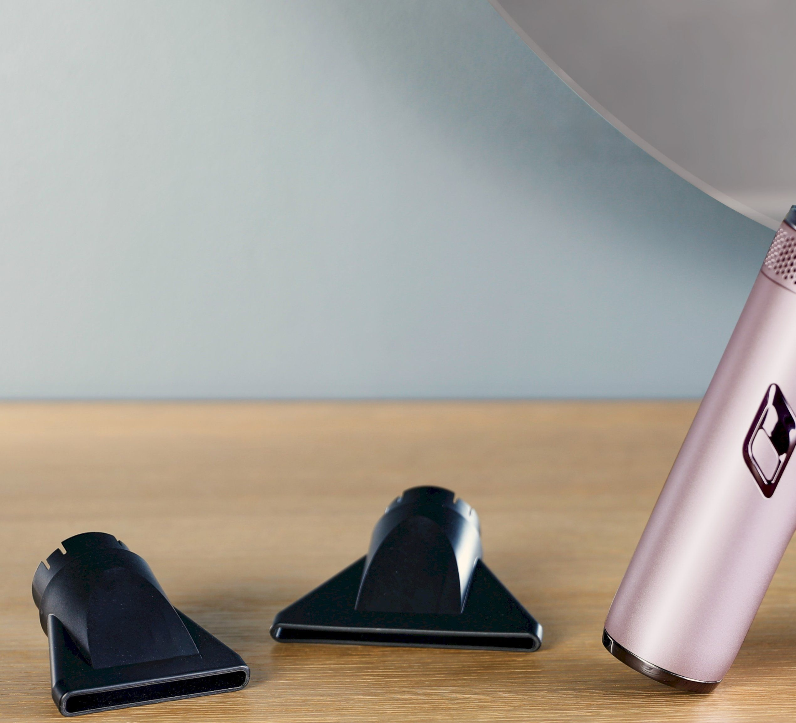 Dwie czarne dysze i różowa suszarka do włosów na drewnie.