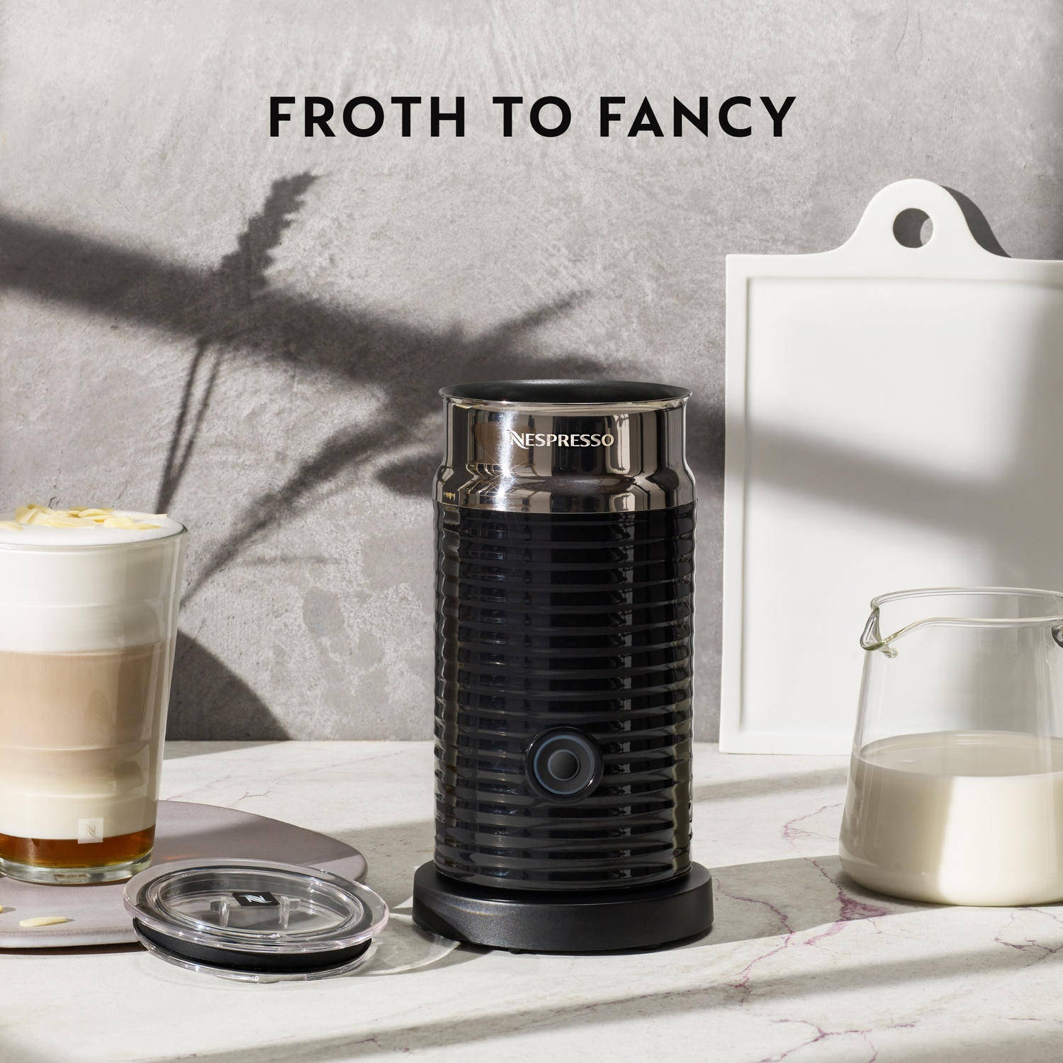 Mousseur à lait Nespresso noir à côté d'un verre de latte et d'un pichet de lait.