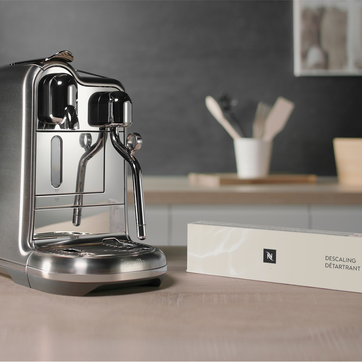 A silver coffee machine sits next to a Nespresso descaling box.