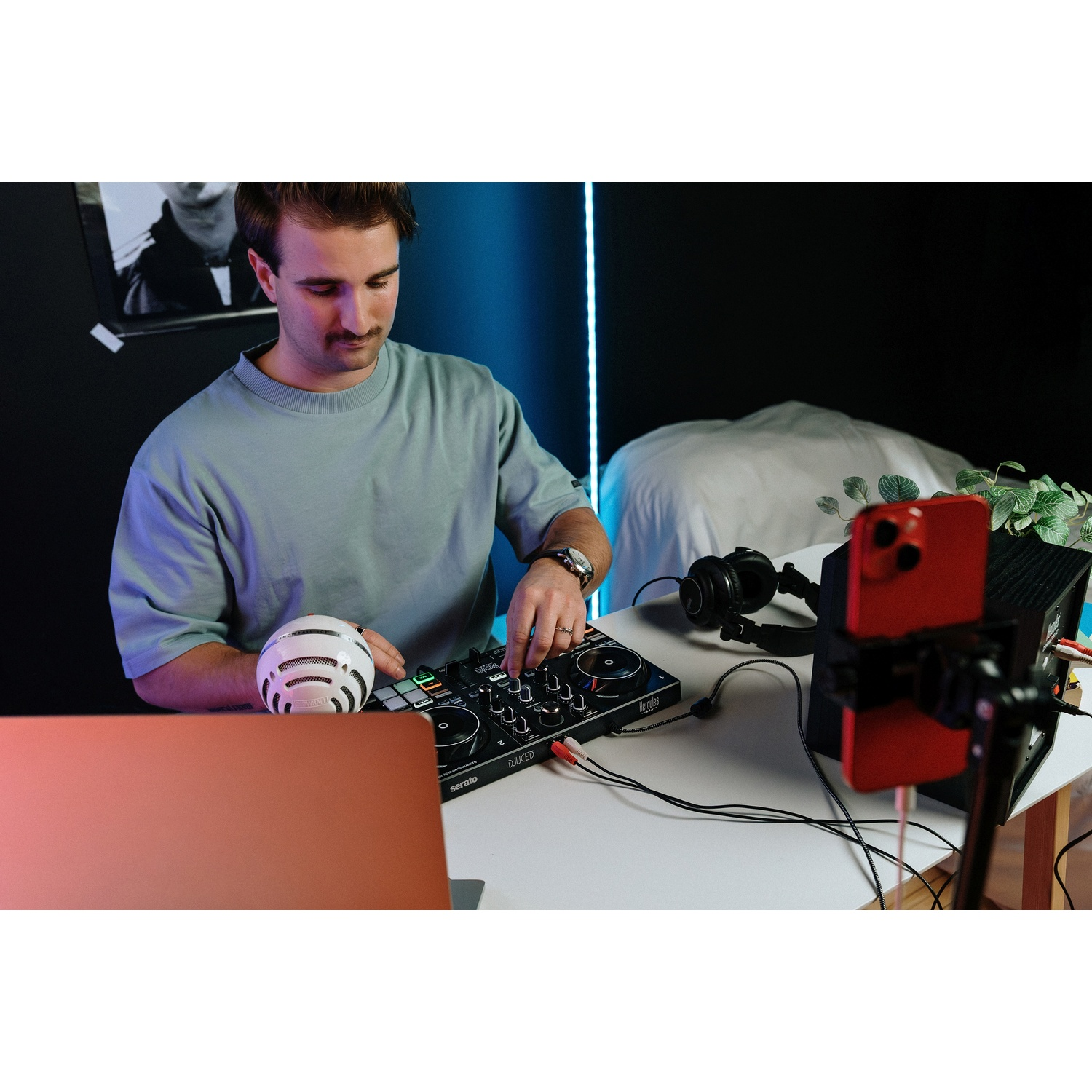 Een man met snor bedient een DJ-setup met laptop, microfoon en telefoon.