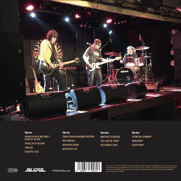Band spielt live auf einer Bühne vor einem Publikum, mit Lautsprechern im Vordergrund.