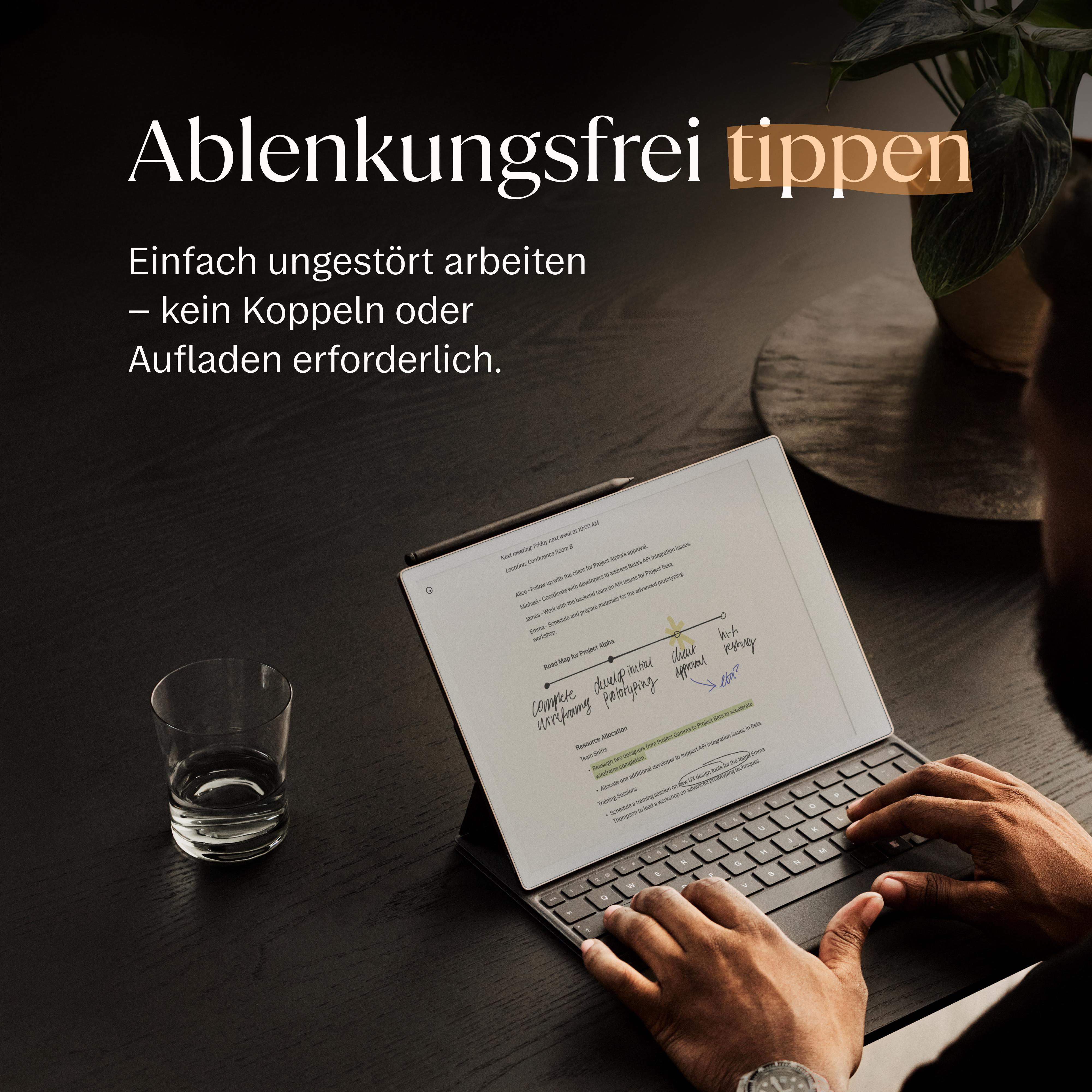 Person tippt auf einem Tablet mit Tastatur, ein Glas Wasser steht daneben.