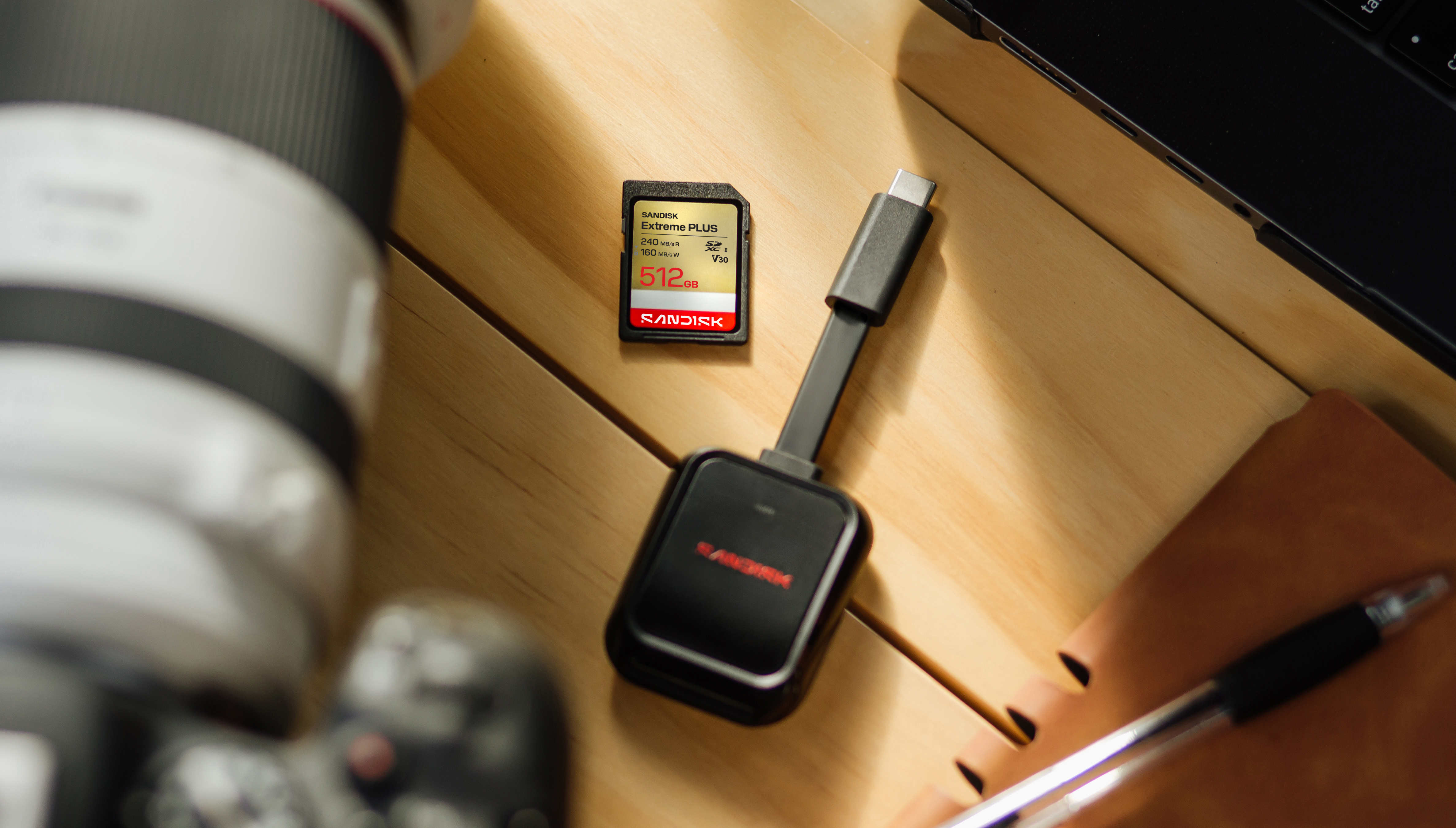 Sandisk 512GB SD Karte mit Kartenleser, Kameraobjektiv und Notizbuch.