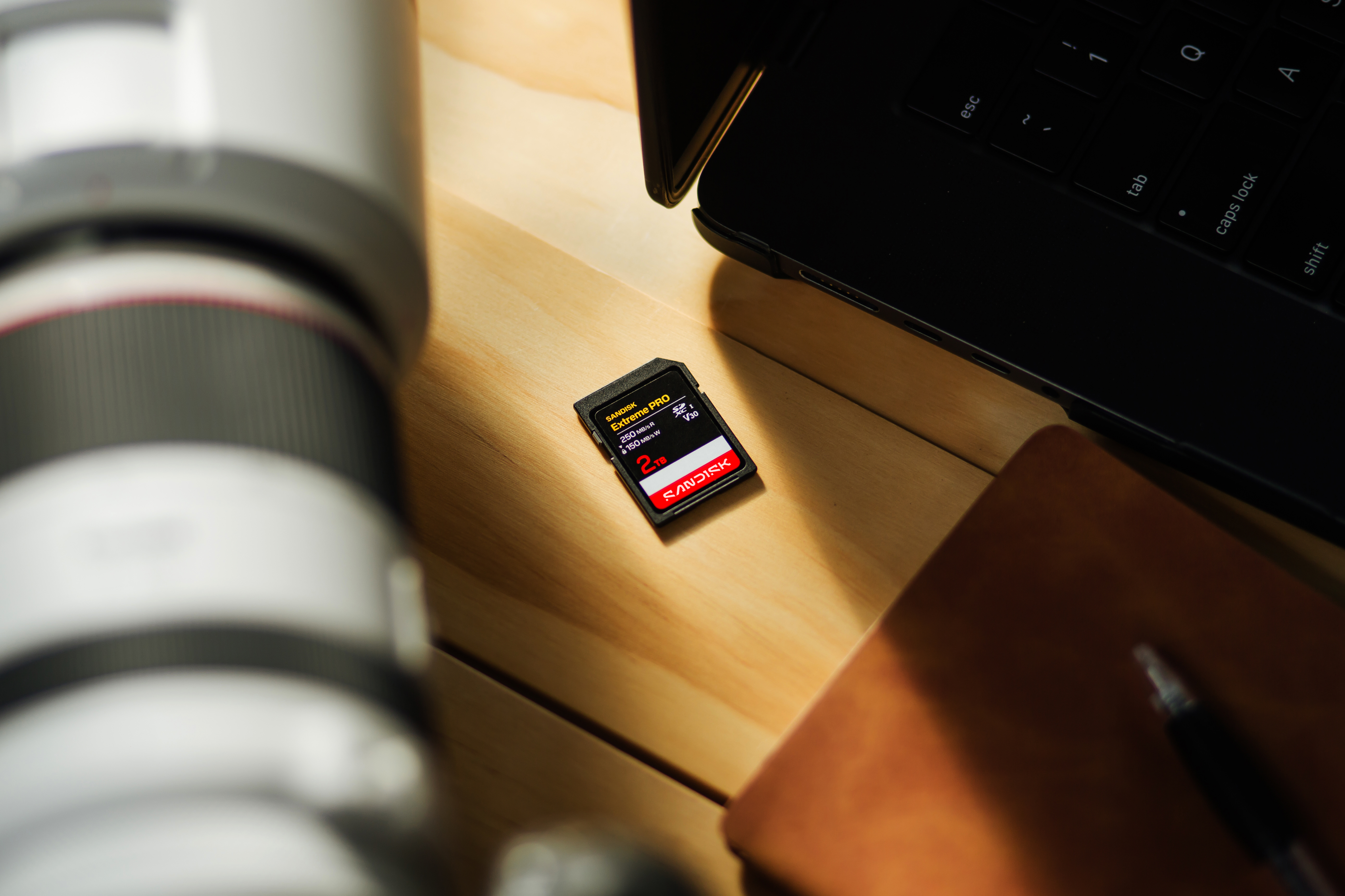 Ein Sandisk 2TB Speicherkarte liegt neben einem Laptop auf einem Holztisch.
