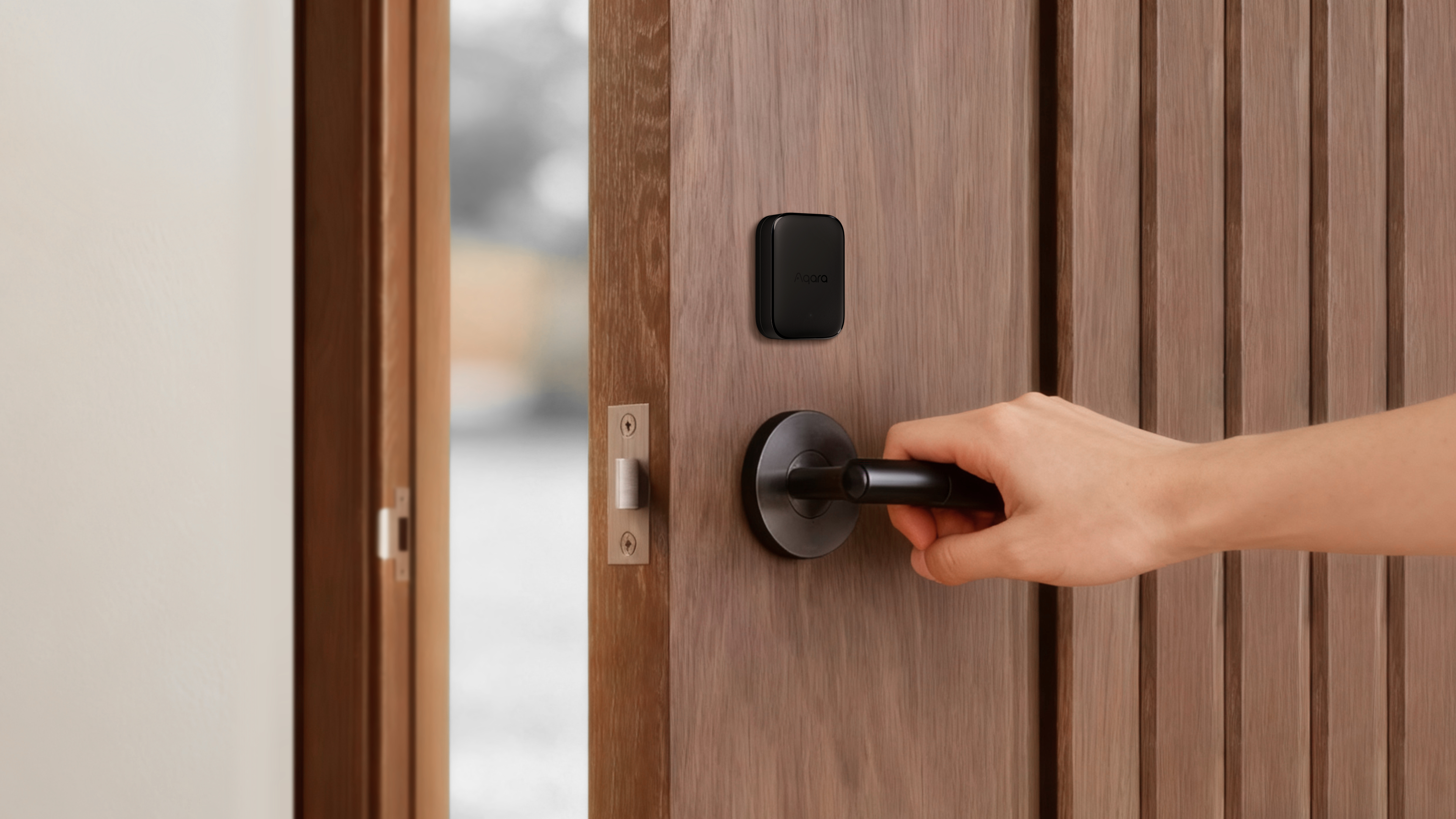 Hand dreht dunklen Türgriff, schwarzer Sensor am Holz. Offene Tür.
