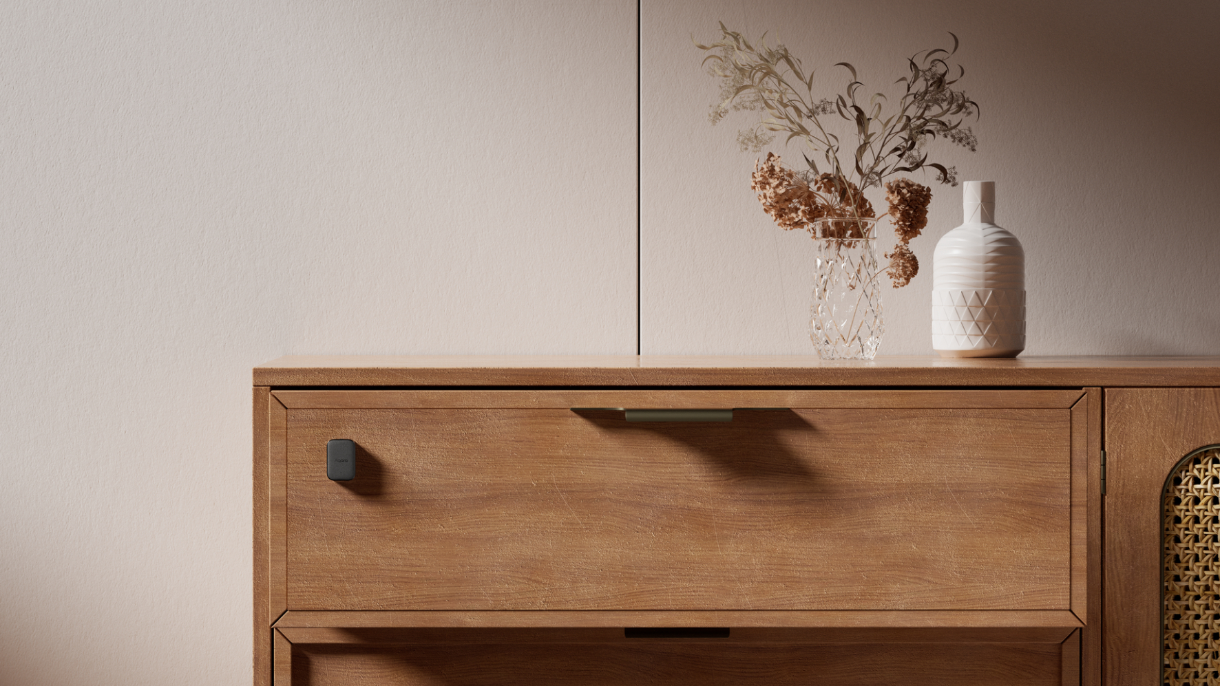 Holzkommode mit zwei Schubladen und einer Tür mit Rattanfront. Vase mit Trockenblumen und weiße Vase.