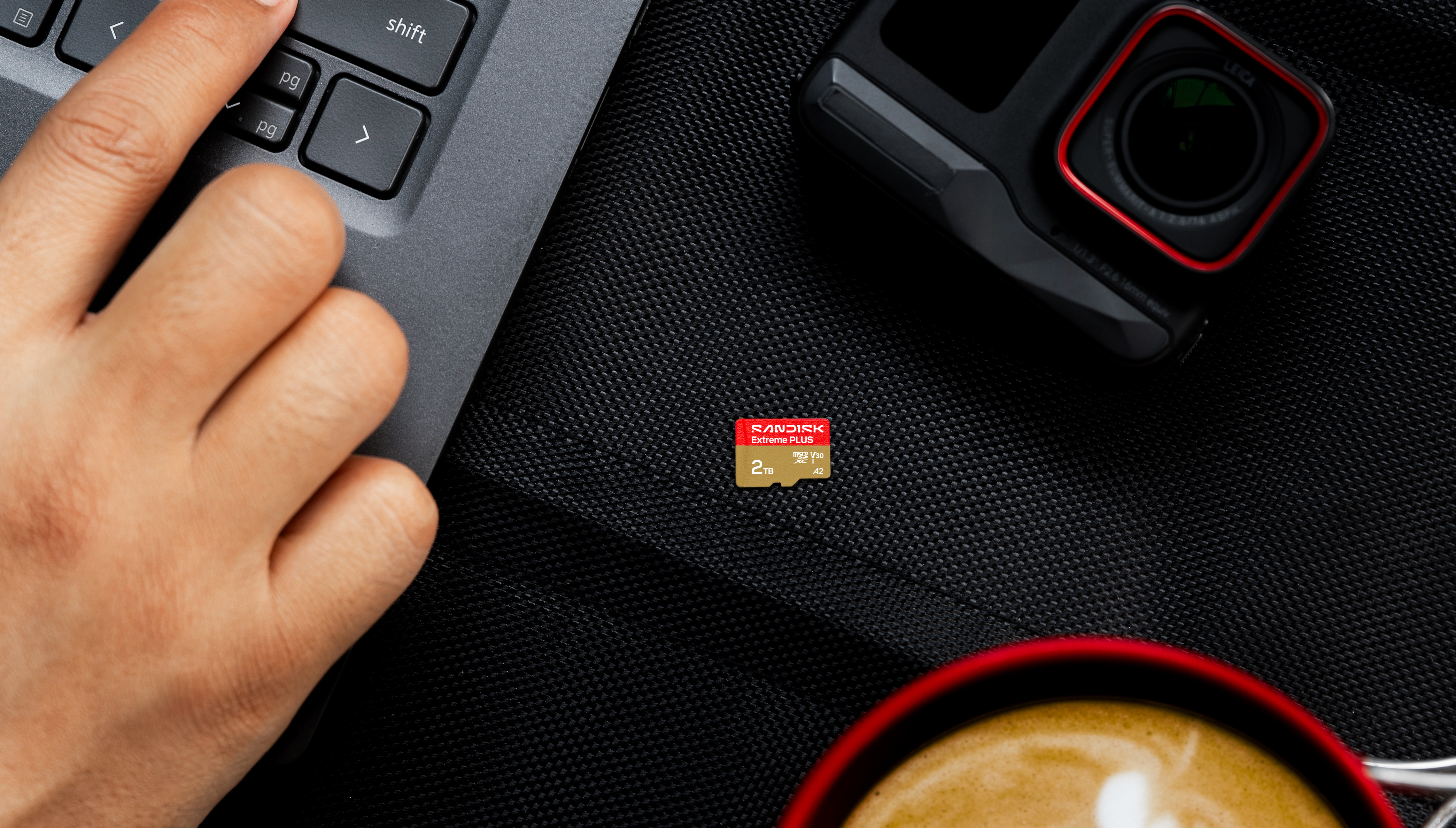 Eine Hand tippt auf einem Laptop in der Nähe einer Kamera, SD-Karte und Kaffee.