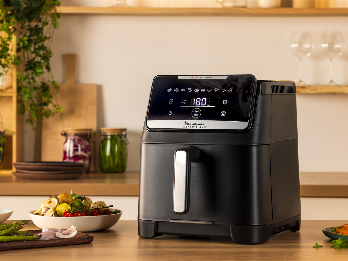 Ein schwarzer Moulinex Heißluftfritteuse mit digitalen Anzeigen steht auf einem Holztisch.