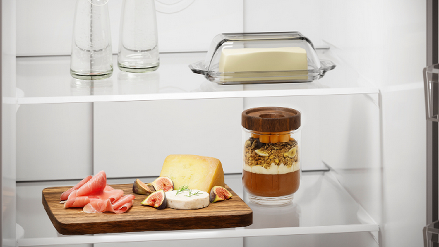 Un estante de refrigerador con jamón, queso, higos, yogur y mantequilla.