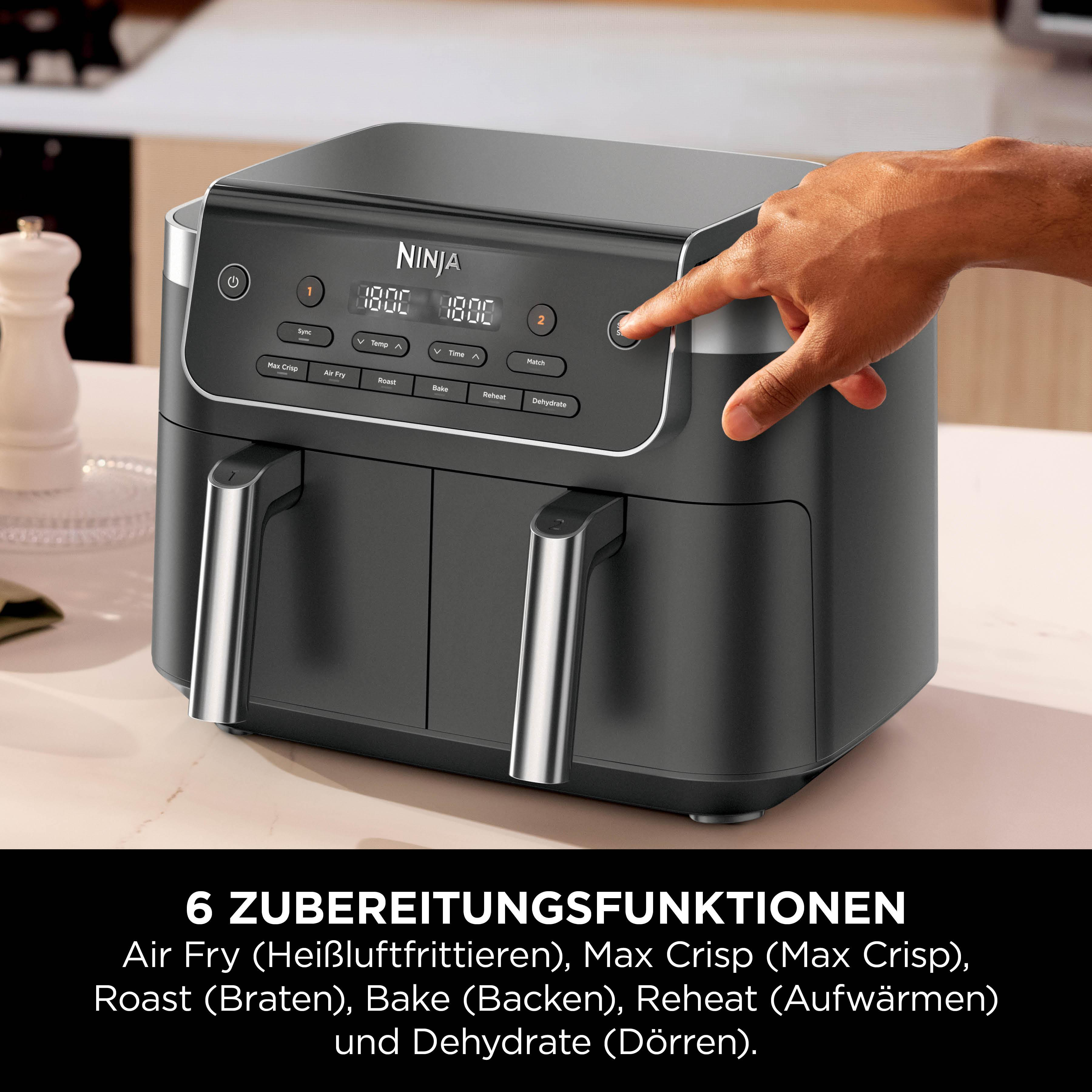 Ein Ninja Heißluftfritteuse mit zwei Körben, eine Hand drückt den Startknopf.