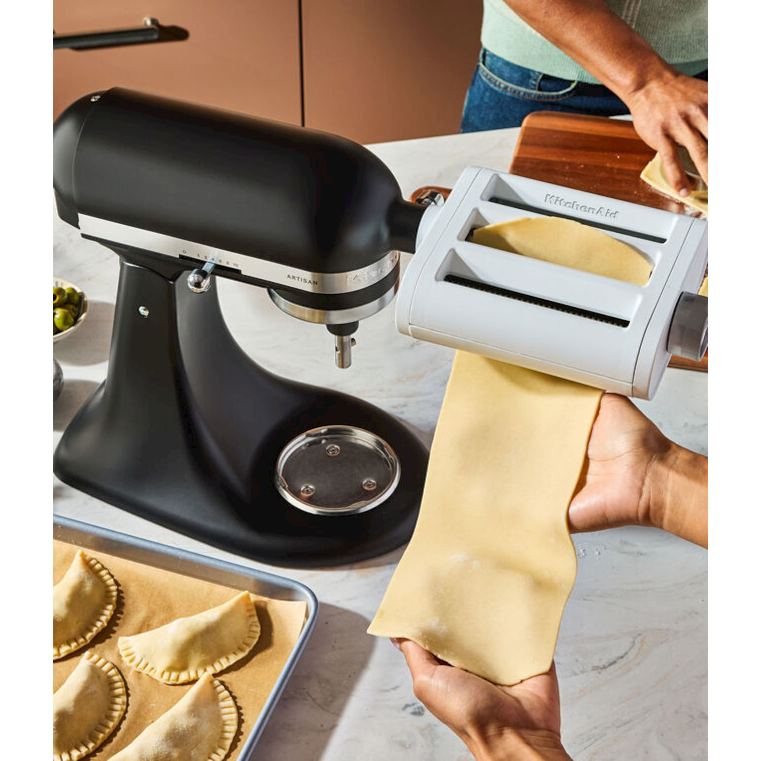 Accessorio nero per planetaria fa pasta, accanto a ravioli ripieni su teglia.