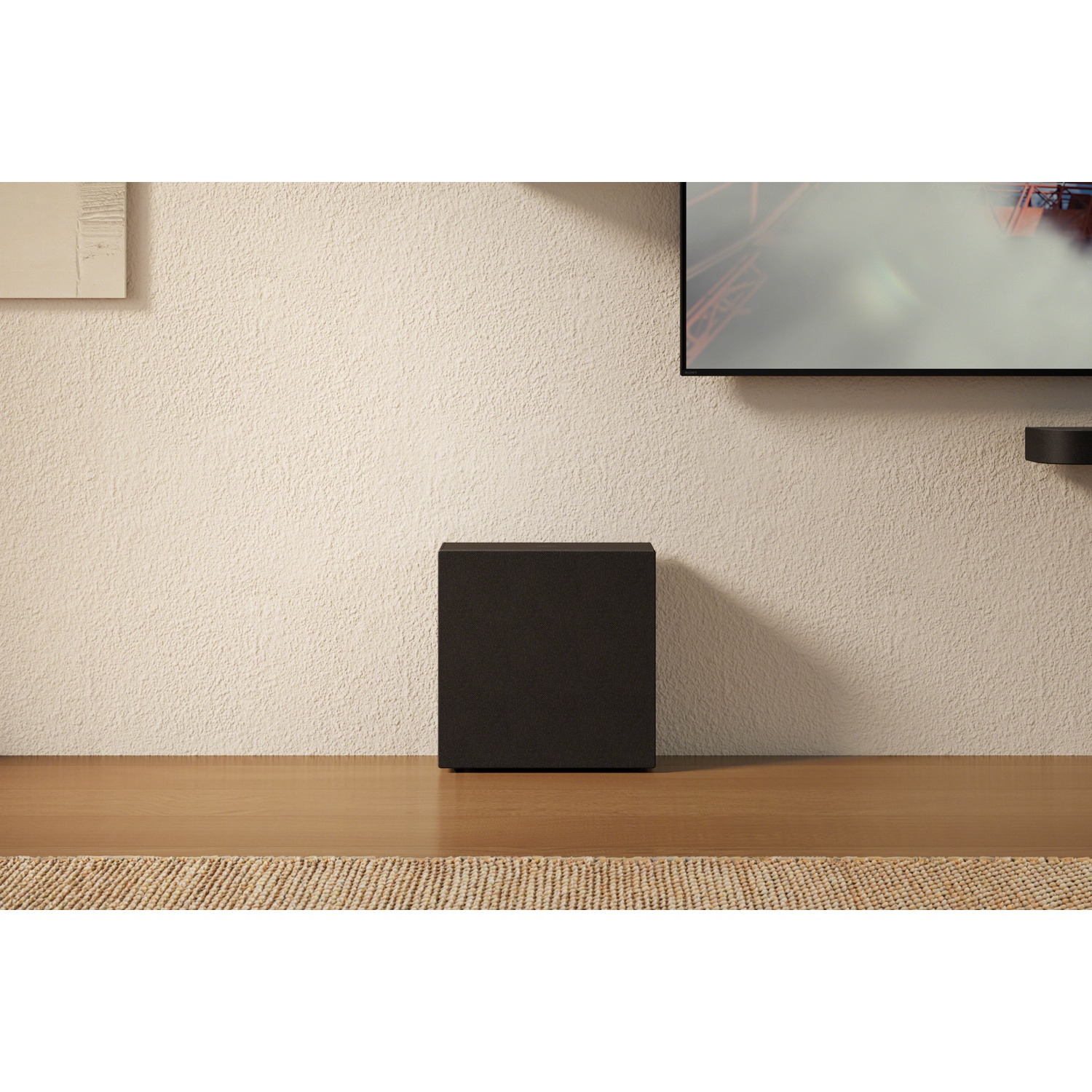 Un caisson de basses noir sur une table en bois devant un mur crème et une télévision.