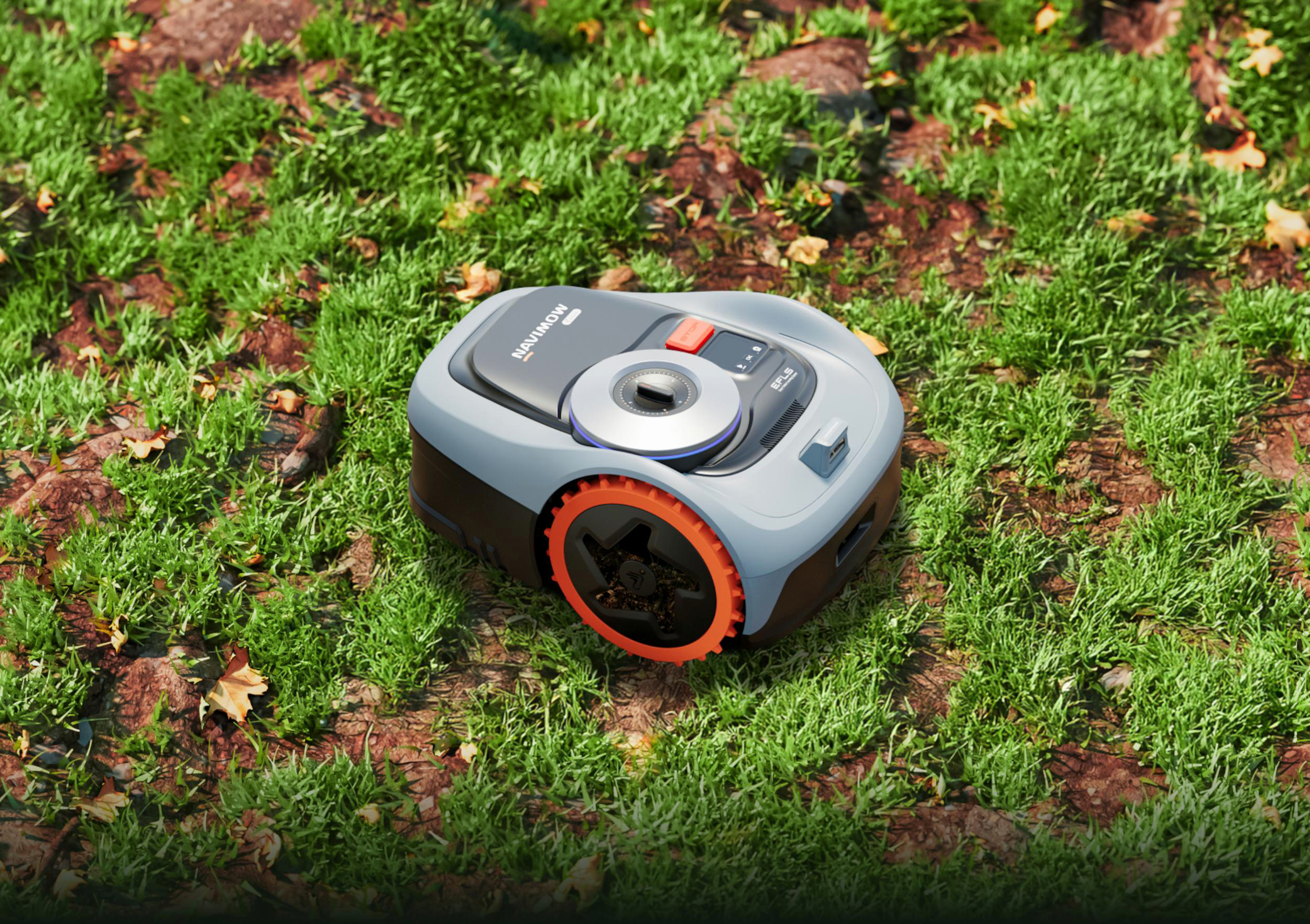 Ein grauer Mähroboter mit orangen Rädern steht auf einem Grasgrund mit Blättern.