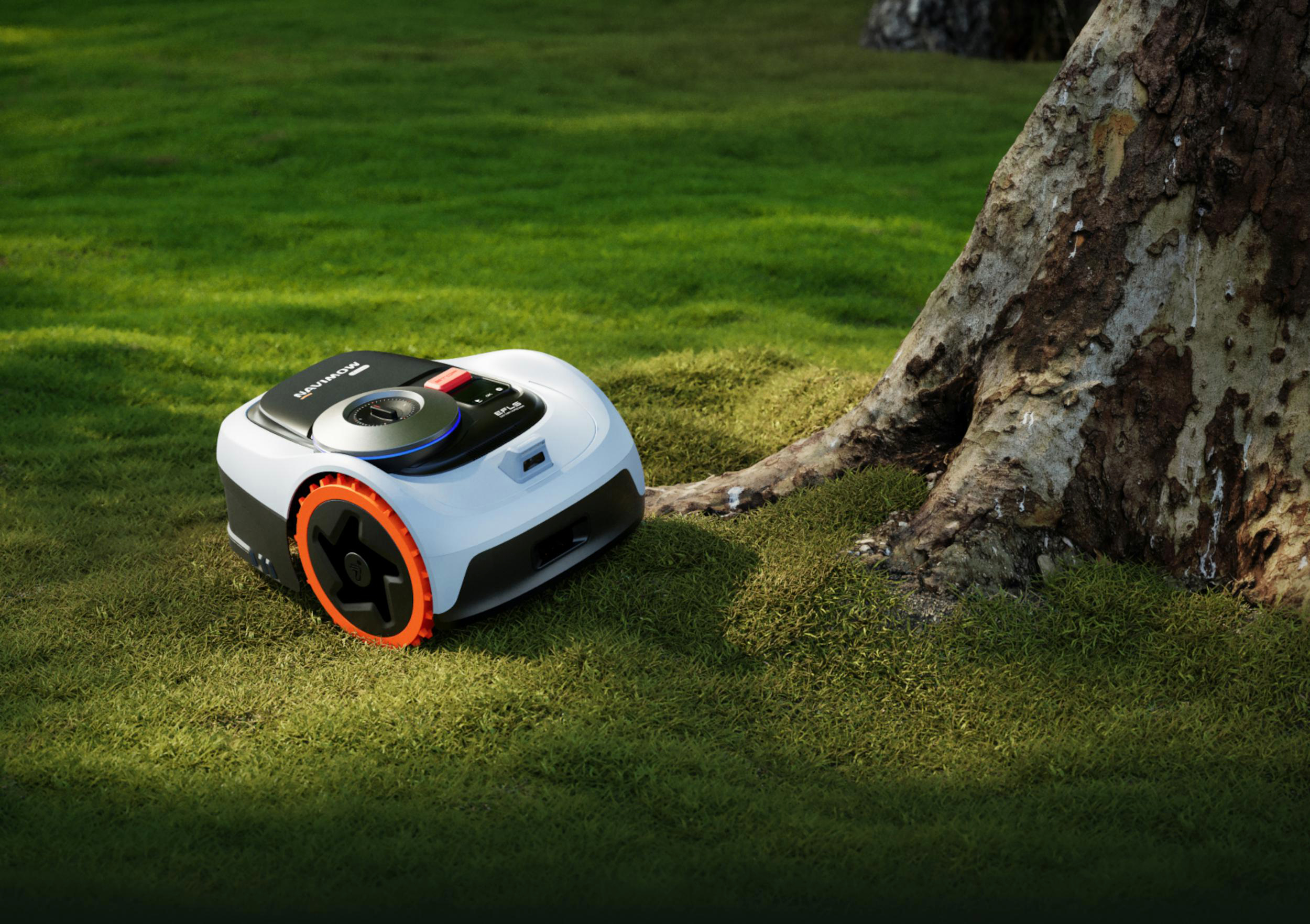 Ein weißer Mähroboter mit orangefarbenen Rädern steht auf einem grünen Rasen neben einem Baumstamm.