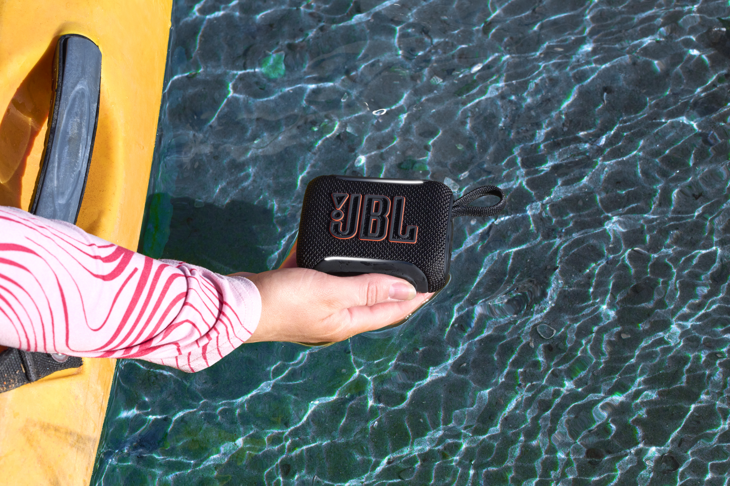 Eine Hand hält einen schwarzen JBL-Lautsprecher im klaren Wasser.