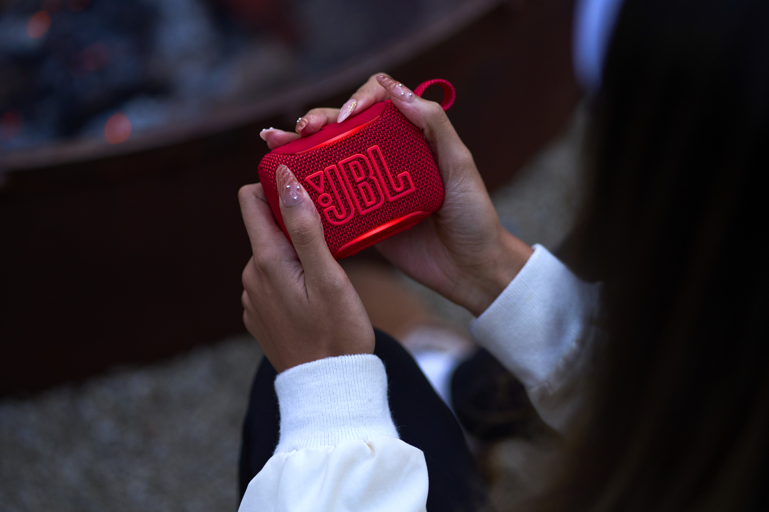 Altoparlante JBL rosso tenuto da mani con unghie lunghe. Sfondo sfocato.
